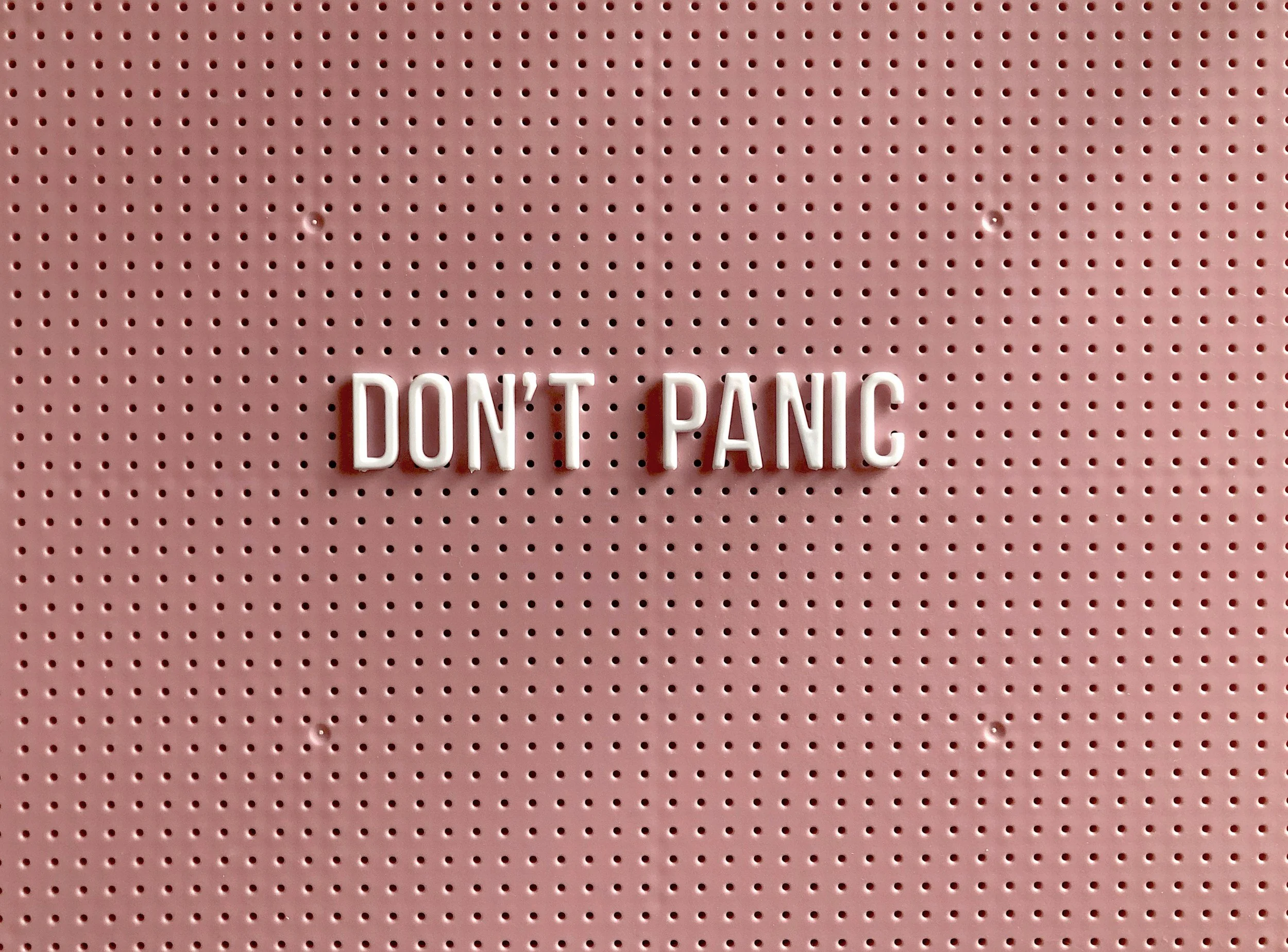 Pink pegboard with white block letters spelling 'DON'T PANIC'.