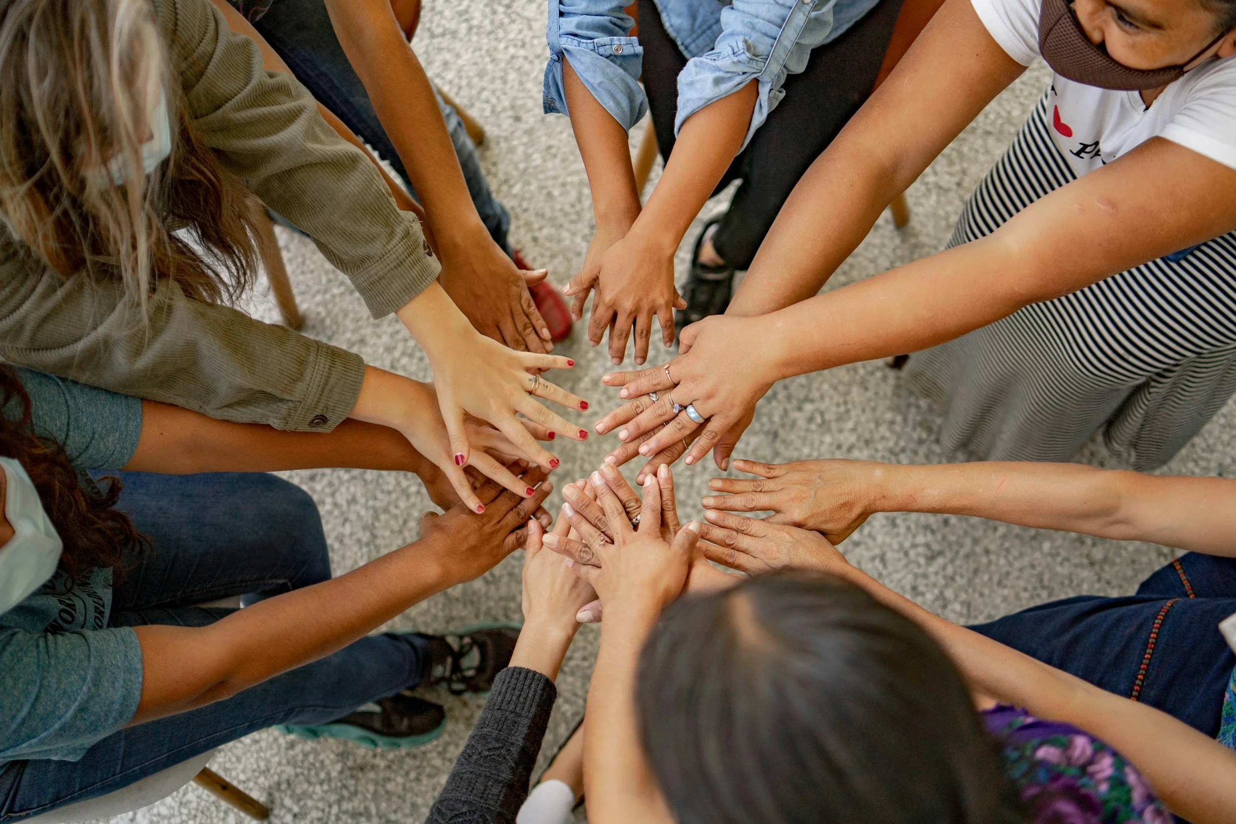 Group of diverse people placing their hands together in the center, symbolizing unity and teamwork.