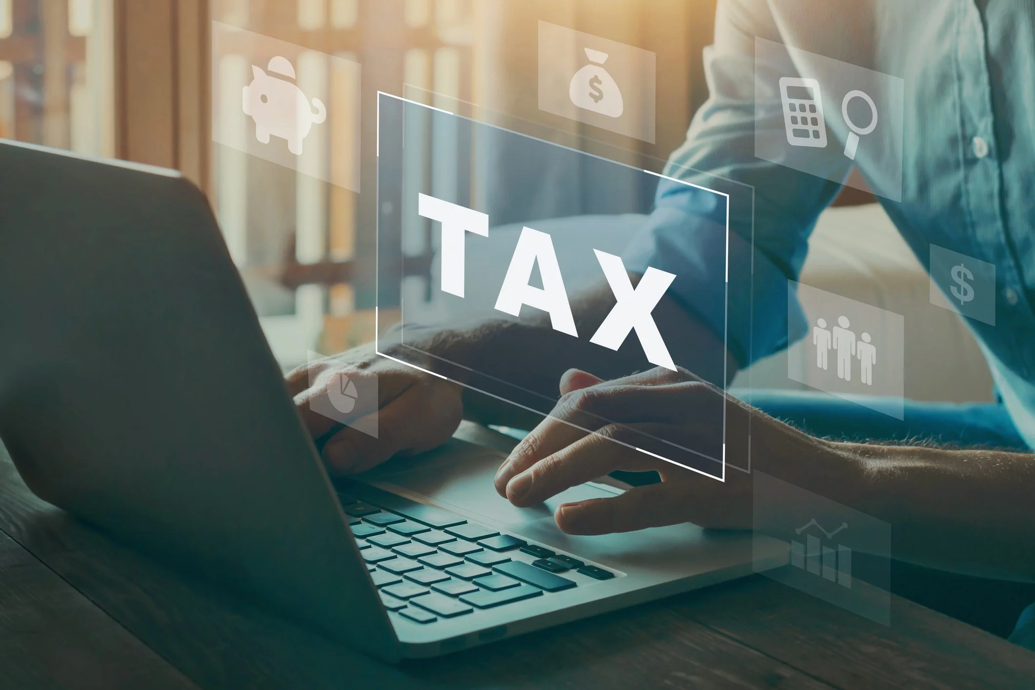 Person using a laptop with digital overlay of the word 'TAX' and various finance icons.