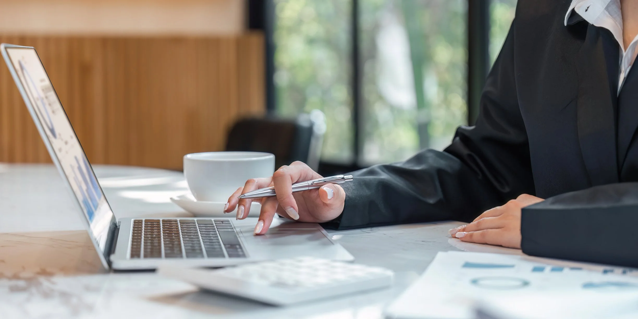 Person using a laptop at a desk with a white mug nearby.