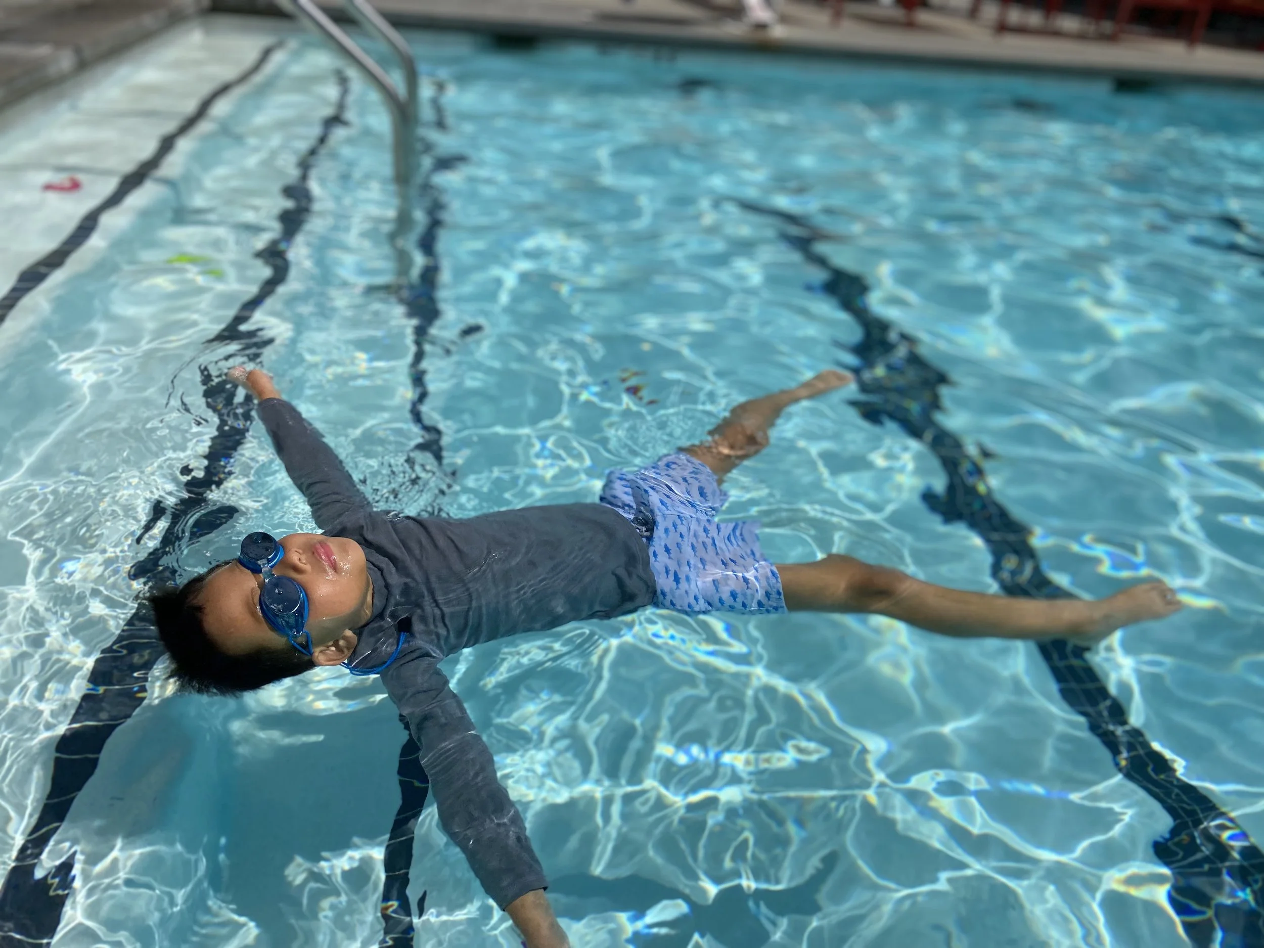Child wearing goggles floating on their back in a swimming pool