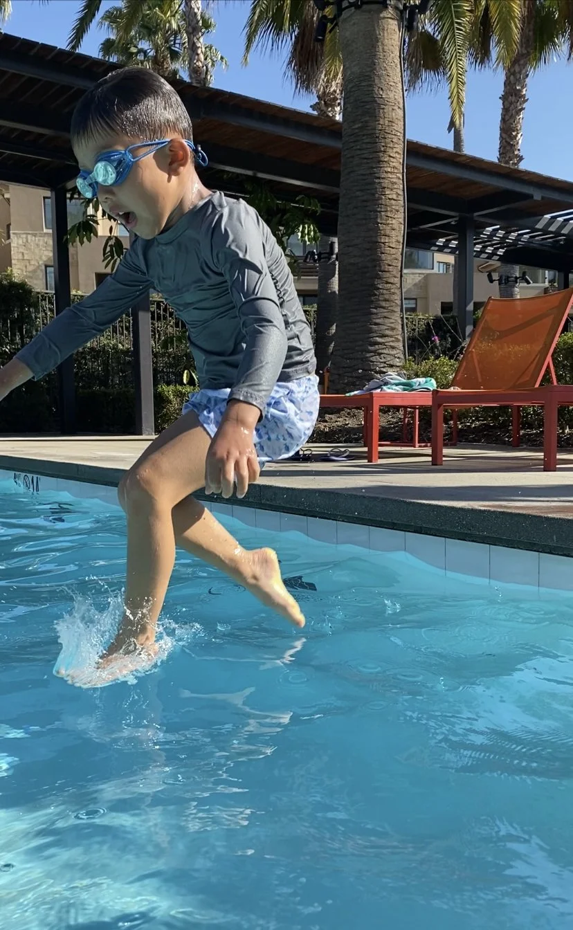 Child jumping into a swimming pool wearing goggles and swimwear.
