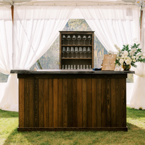 Wooden bar with live-edge top, floral arrangement, and window with white curtains.