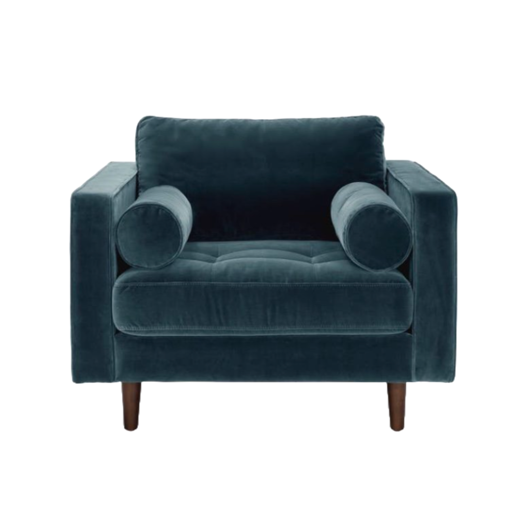 A navy blue velvet armchair with two cylindrical pillows, wooden legs, and a plush seat and backrest, isolated on a white background.