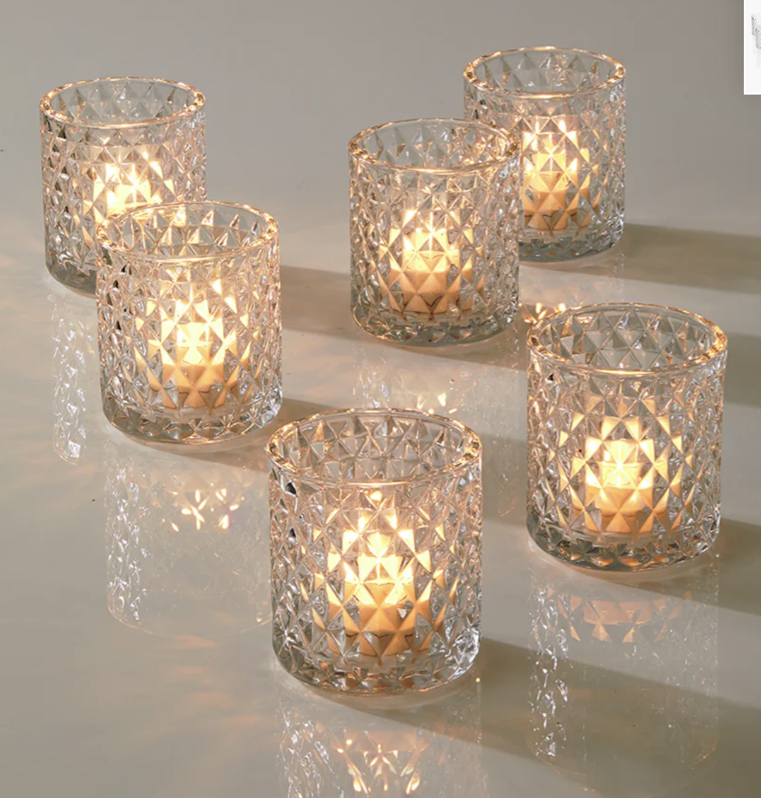 Six lit decorative glass candle holders with diamond-like patterns on a reflective surface.