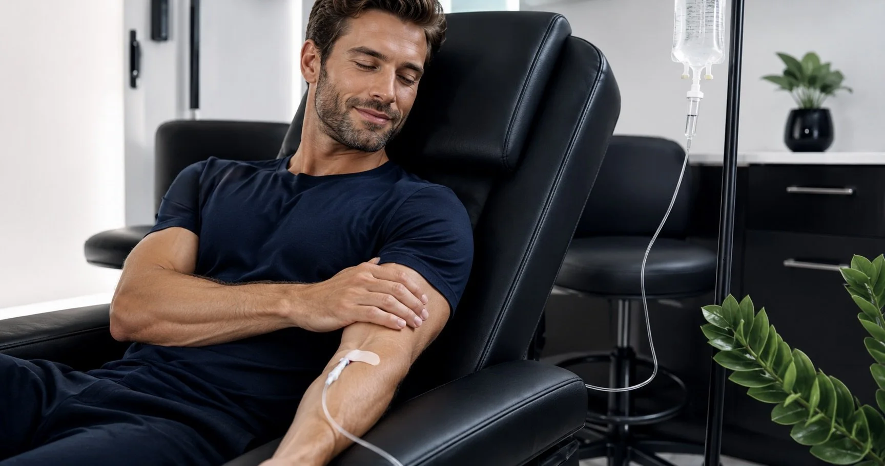 Man smiling and relaxing in a med spa chair, connected to an IV drip with Recovery Cocktail infusion