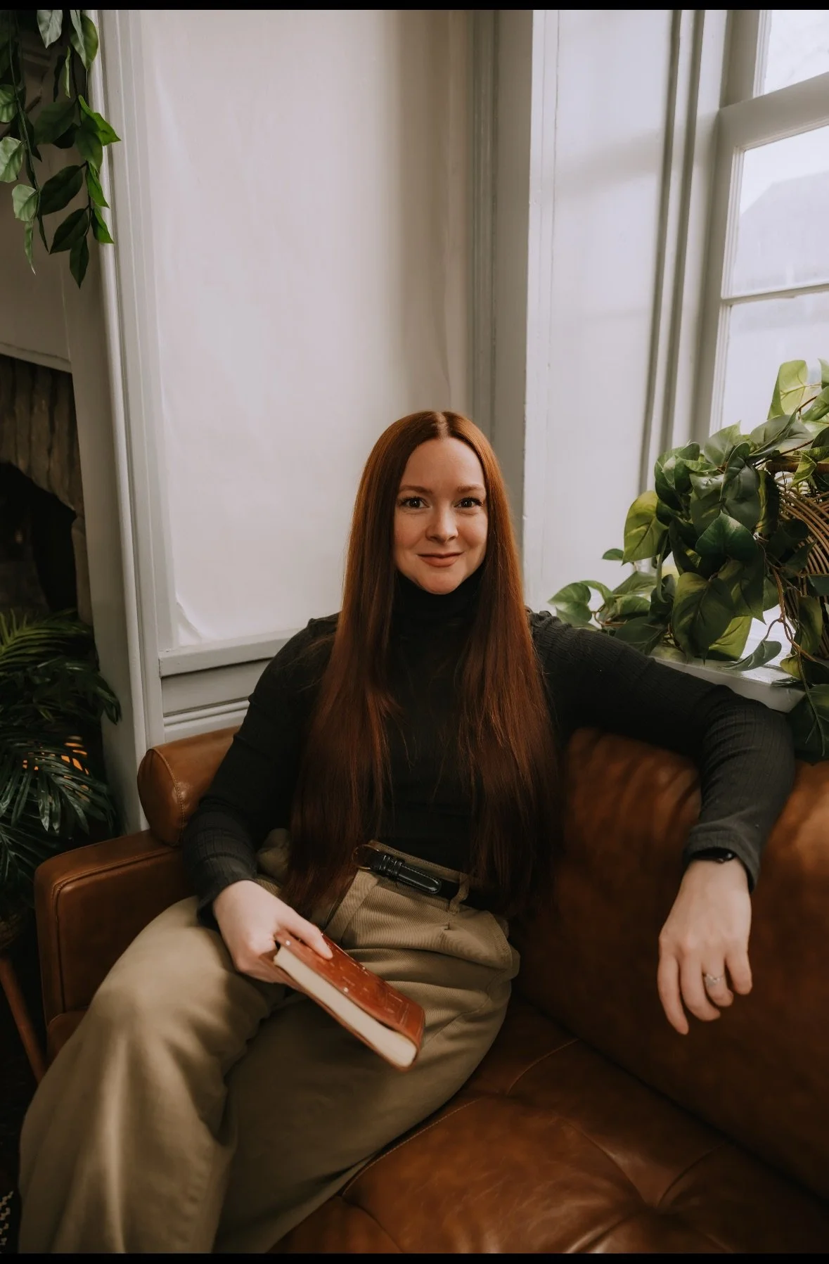 A woman with long red hair smiling in an indoor setting, wearing a black jacket and white shirt.