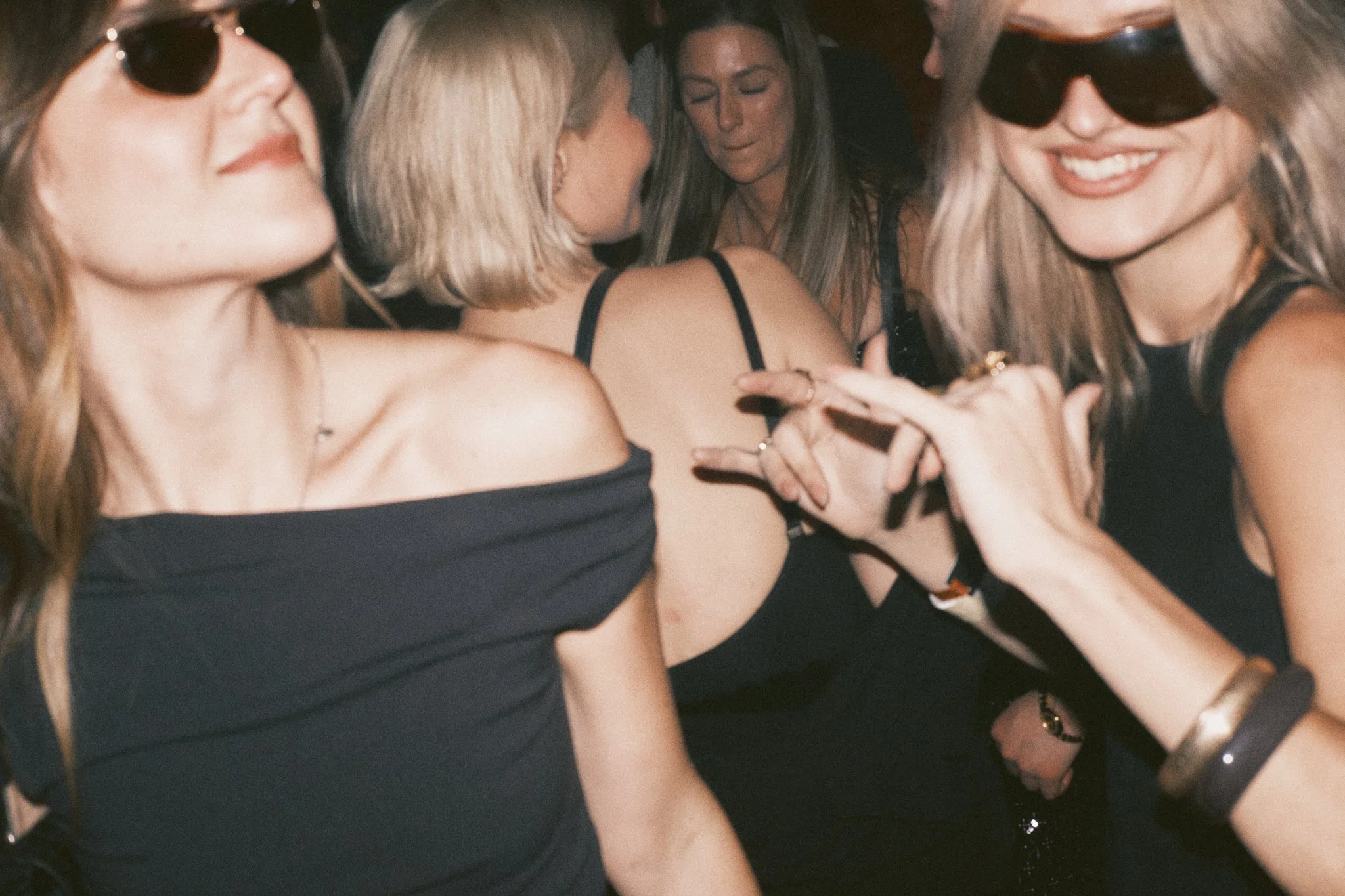 Group of women dancing and socializing at a party, some wearing sunglasses, in a lively setting.