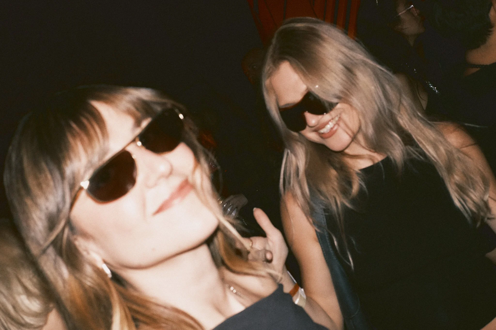 Two women smiling and wearing sunglasses at a social event or party.