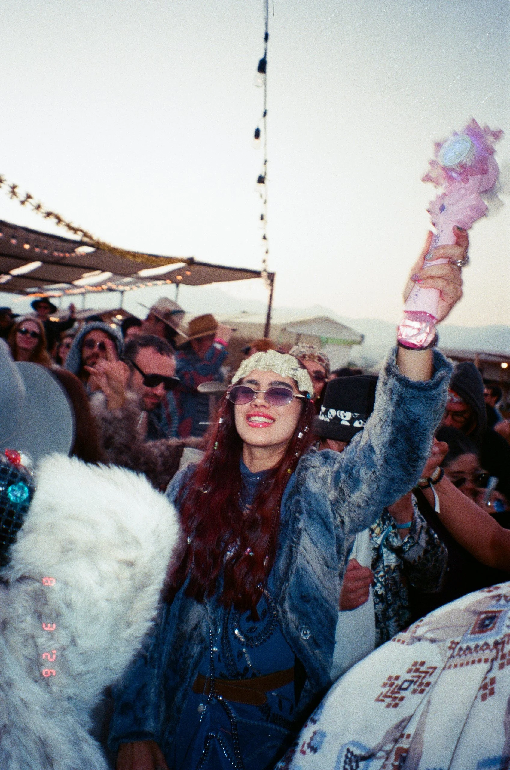 A woman with long red hair, wearing sunglasses and a crown, holding a pink sparklers in the air at Amarás Oaxaca Experience 2026.