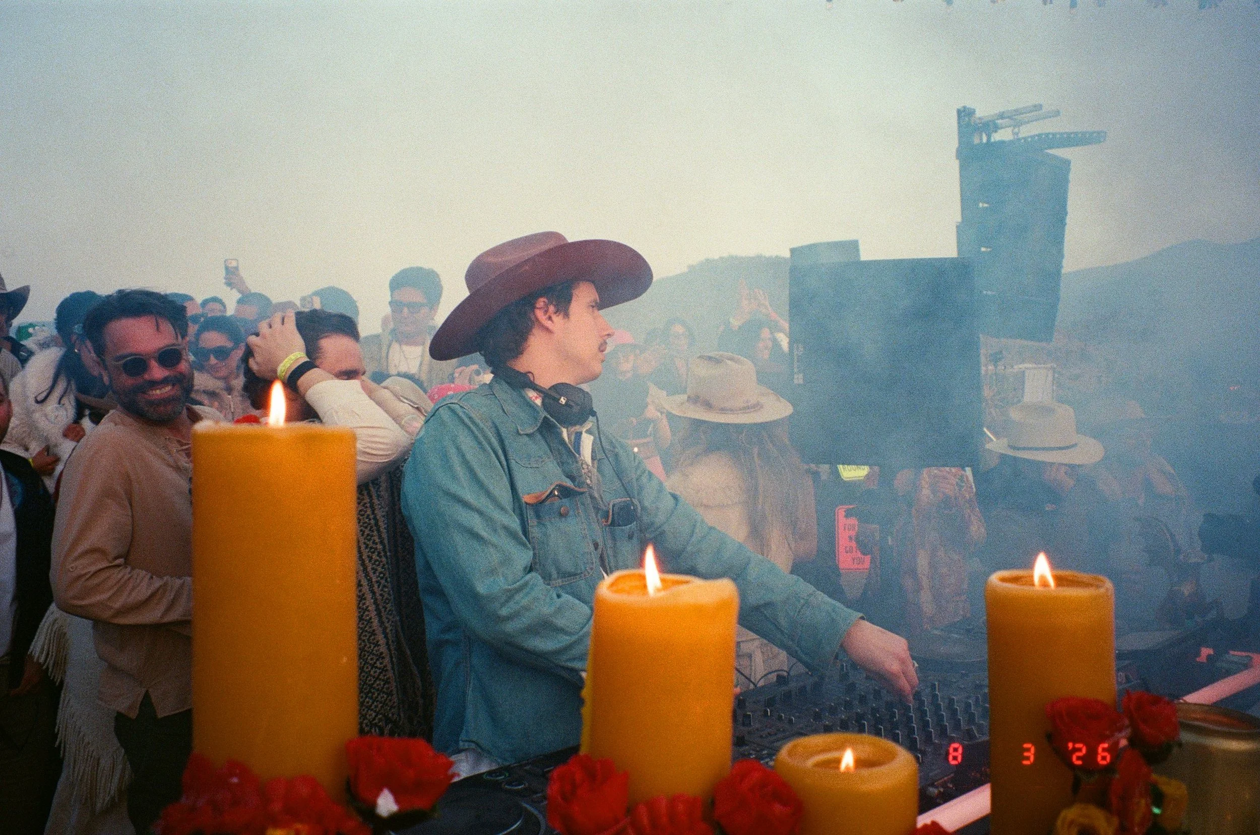 A group of people at Amarás Oaxaca Experience 2026, with candles and flowers in the foreground, and DJ Salimbeni in the foreground wearing a denim jacket and a large wide-brimmed hat.