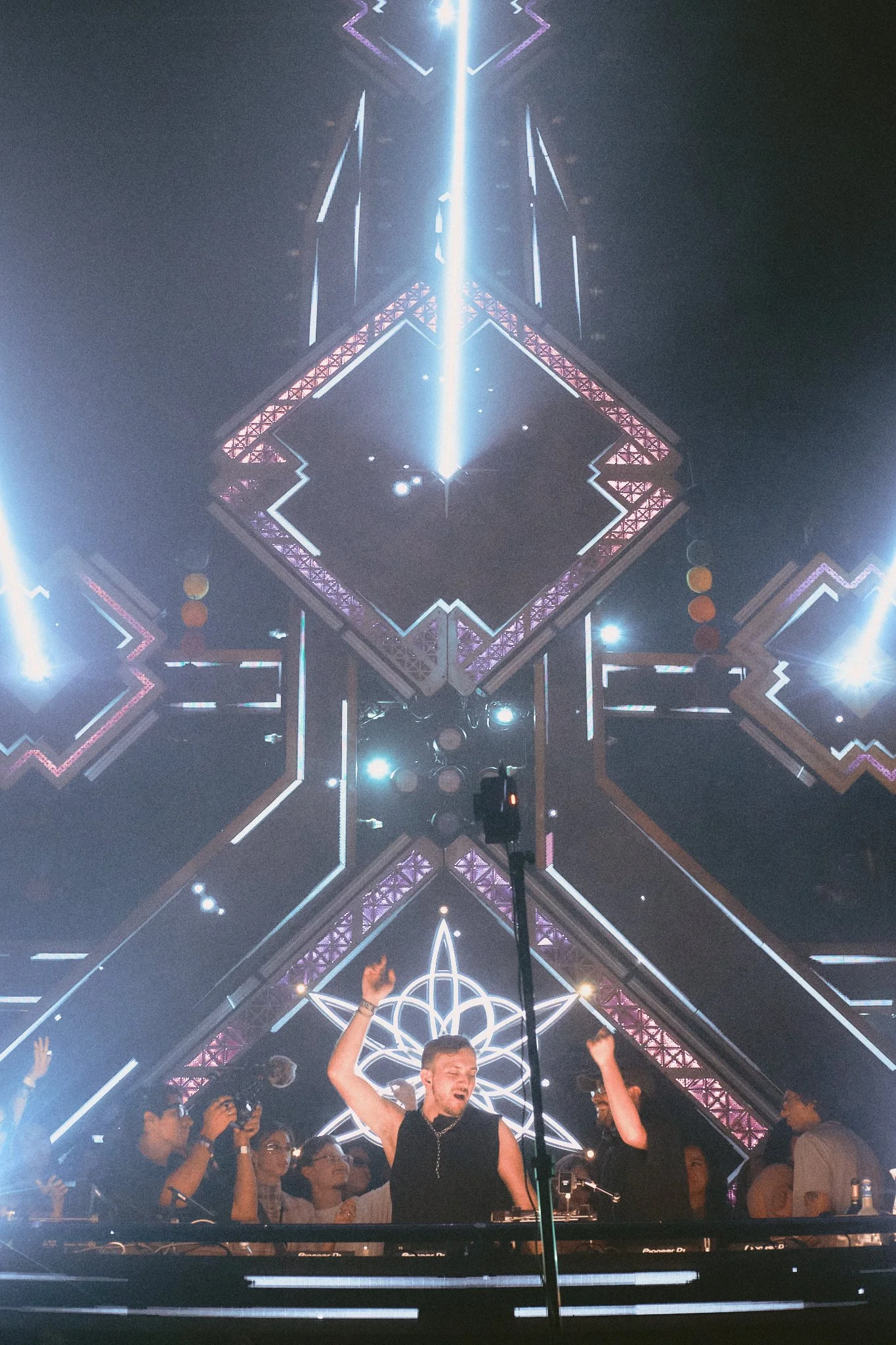 A DJ performing at a nightclub with a decorative geometric light display in the background.