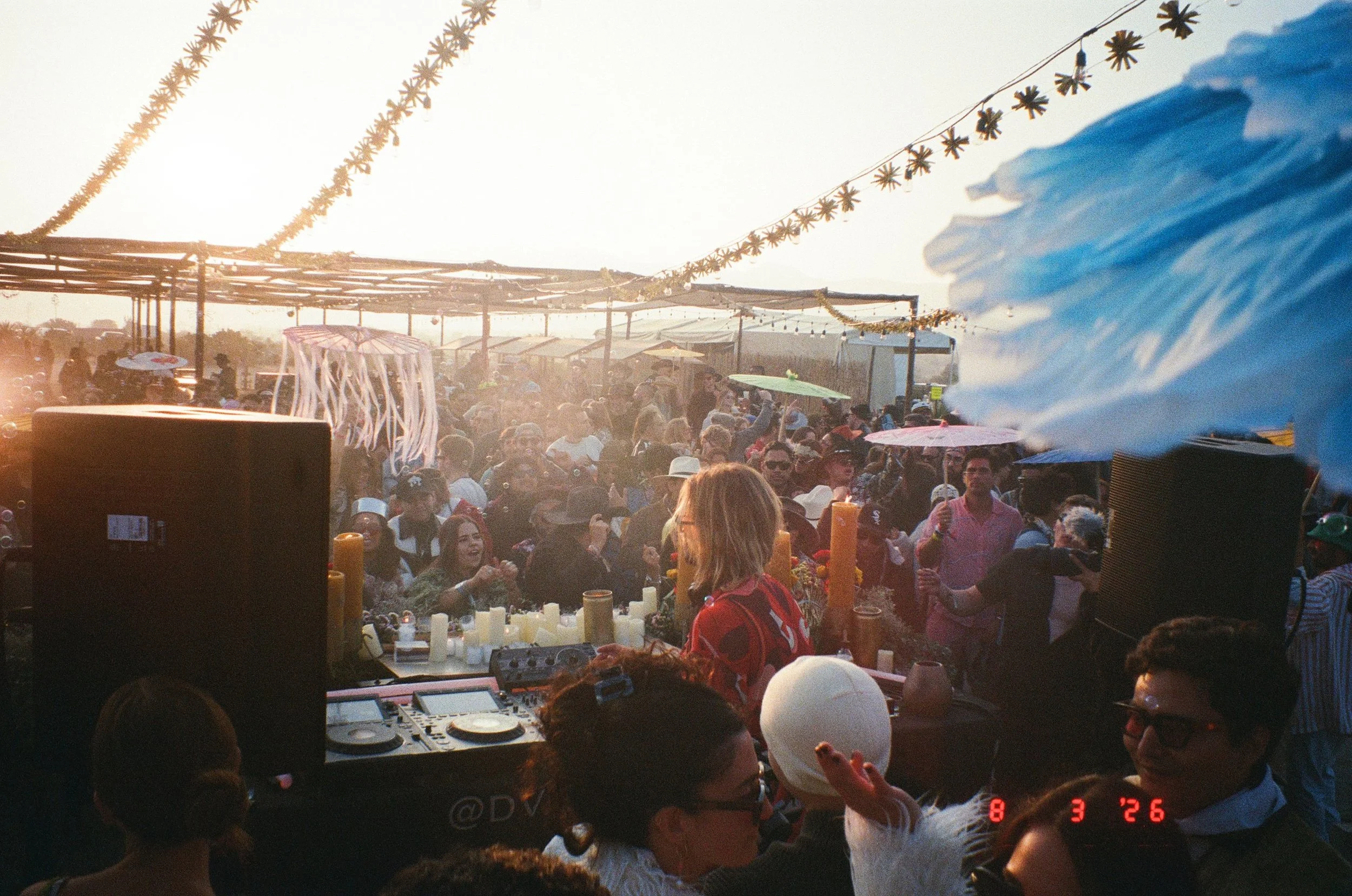 Crowd dancing and socializing at Amarás Oaxaca Experience 2026 with string lights and umbrellas, under a bright, sunny sky.