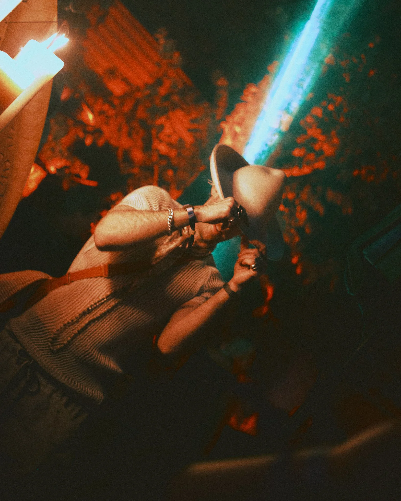 Person holding a hat, facing a blue laser beam in a dark environment with red lighting effects.