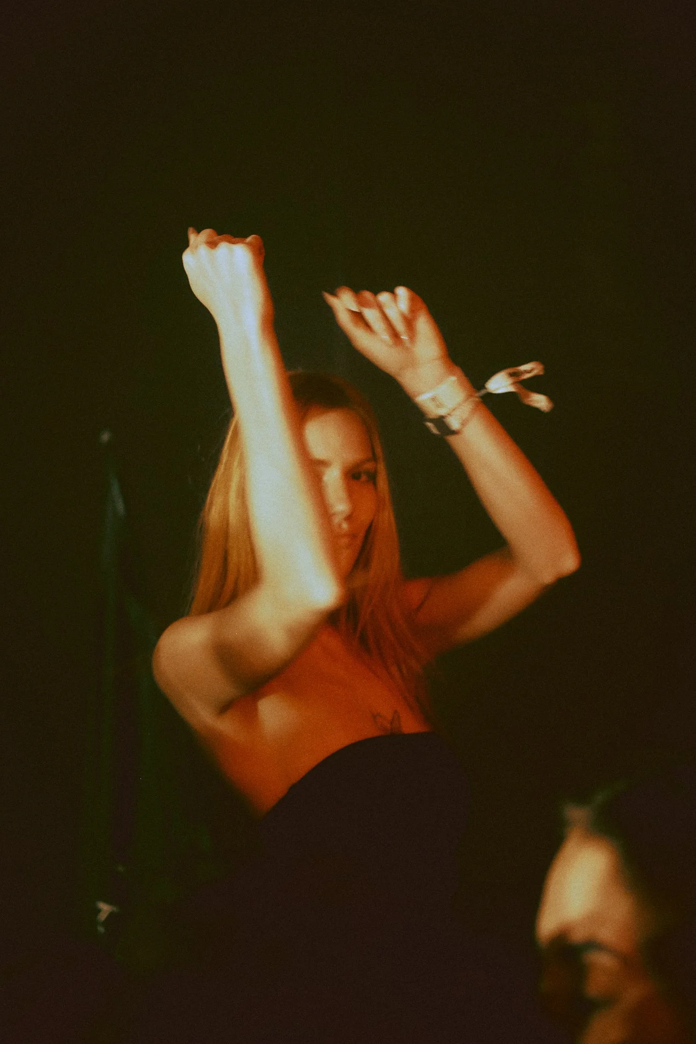 A woman dancing on stage with her arms raised, smiling, in a dark setting.