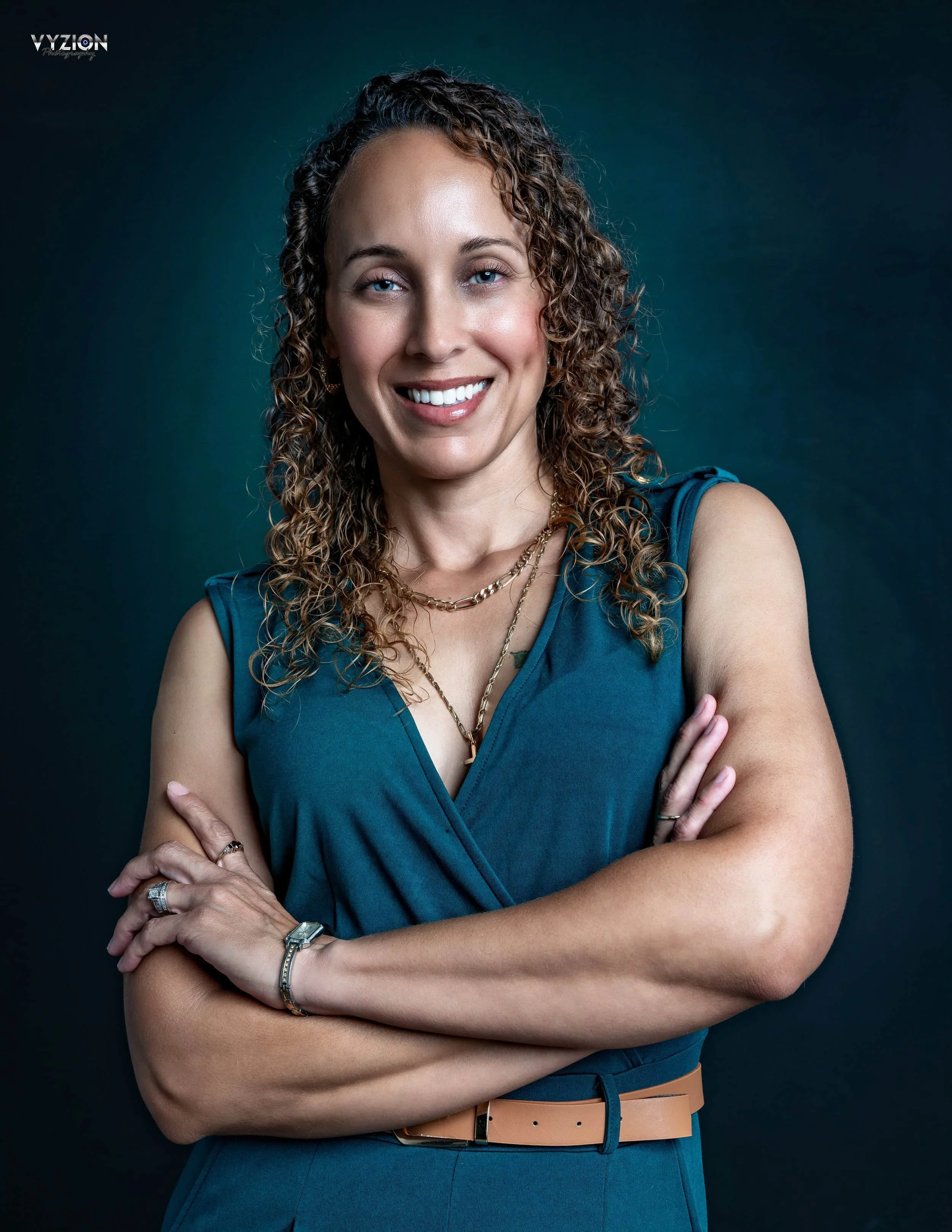 Smiling person with curly hair, wearing a blue sleeveless top and crossed arms