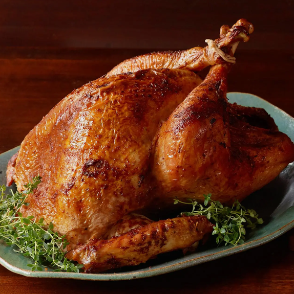 A roasted whole chicken on a platter garnished with herbs.