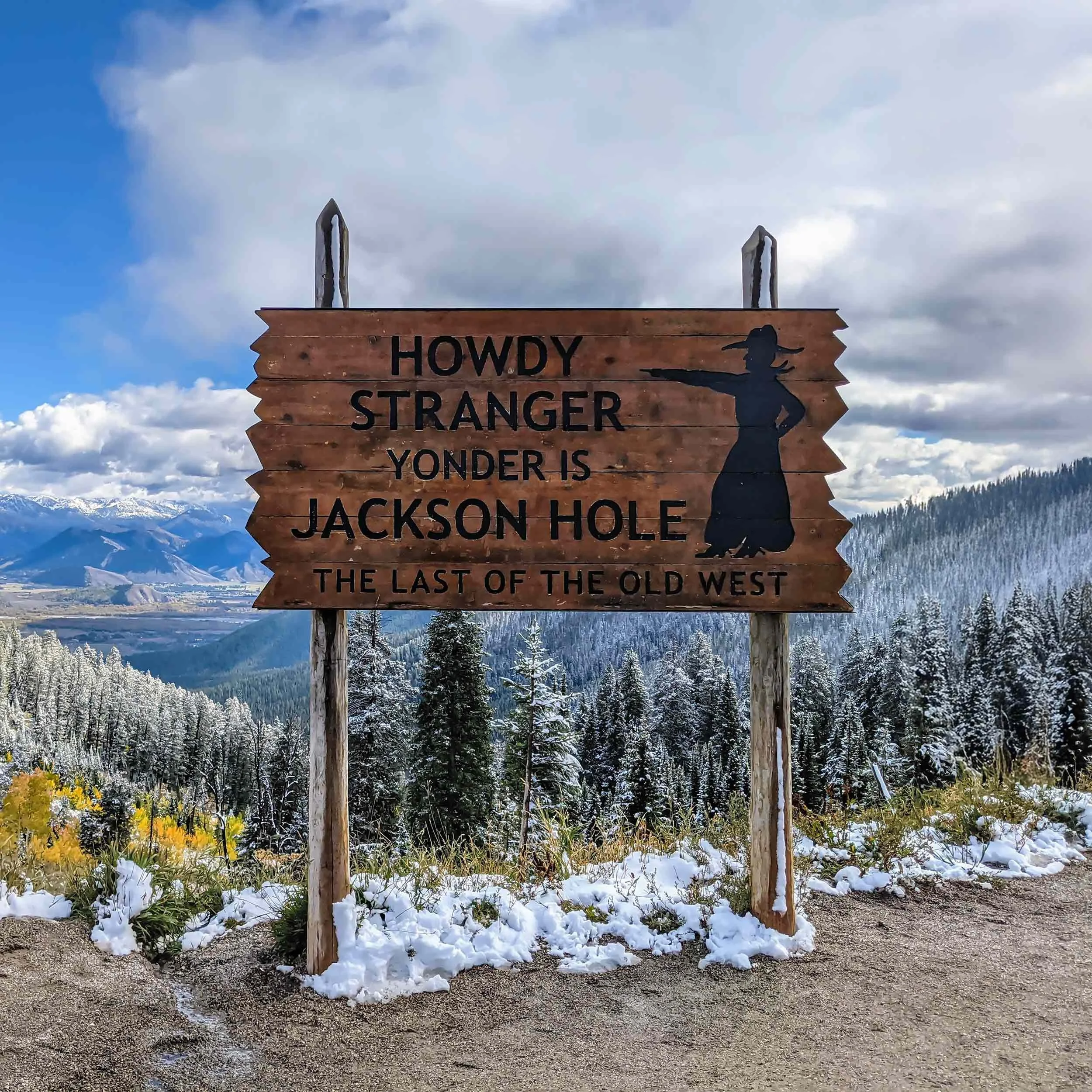 The iconic wooden sign with a silhouette cowboy, pointing to the valley in the distance. The sign reads "Howdy Partner, yonder is Jackson Hole, the last of the old west".