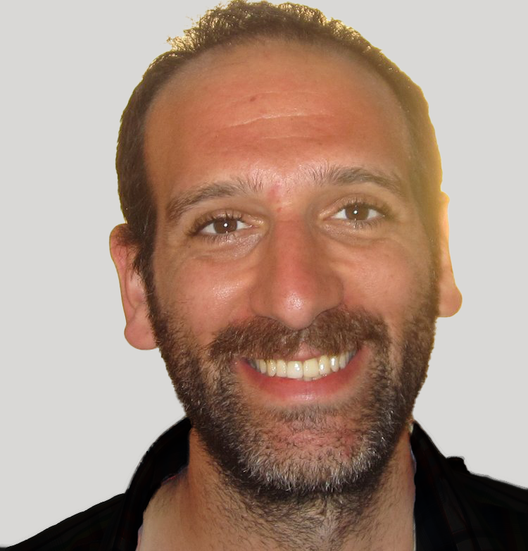 Man smiling with a beard and short hair in front of a light background.