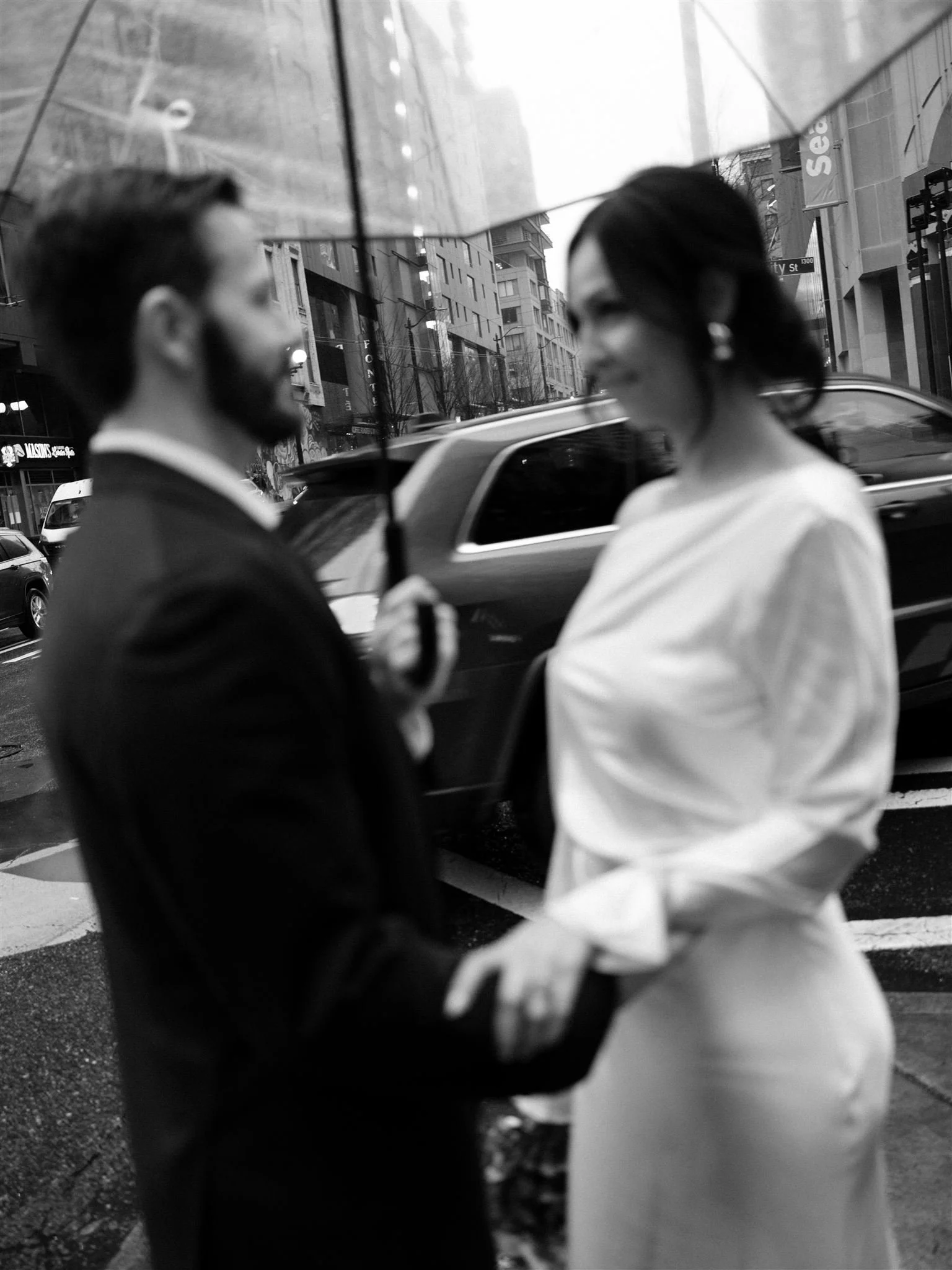Couple sharing a quiet moment under an umbrella outside the Seattle Municipal Courthouse on a rainy day, photographed in black and white in downtown Seattle.