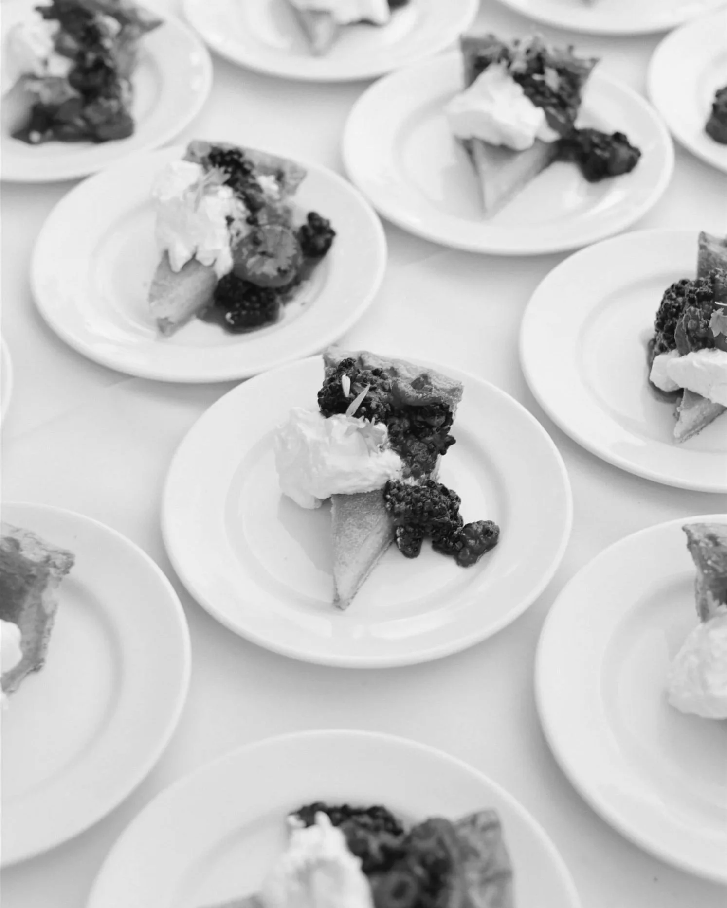 Multiple plates with slices of pie topped with whipped cream and blackberries, arranged on a table.