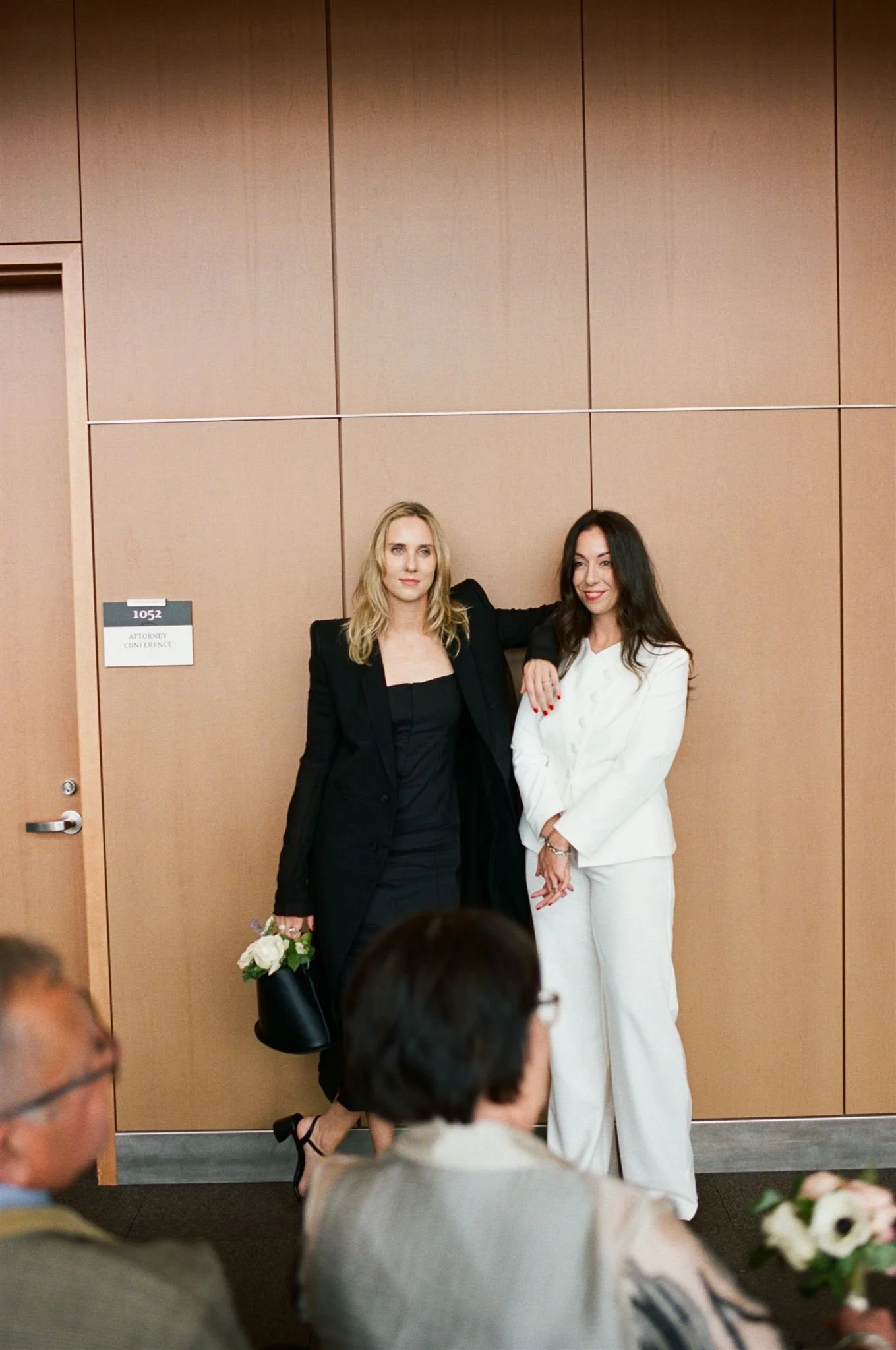 ame-sex couple standing together inside the Seattle Municipal Courthouse, dressed in modern black and white suits during an intimate courthouse wedding ceremony.