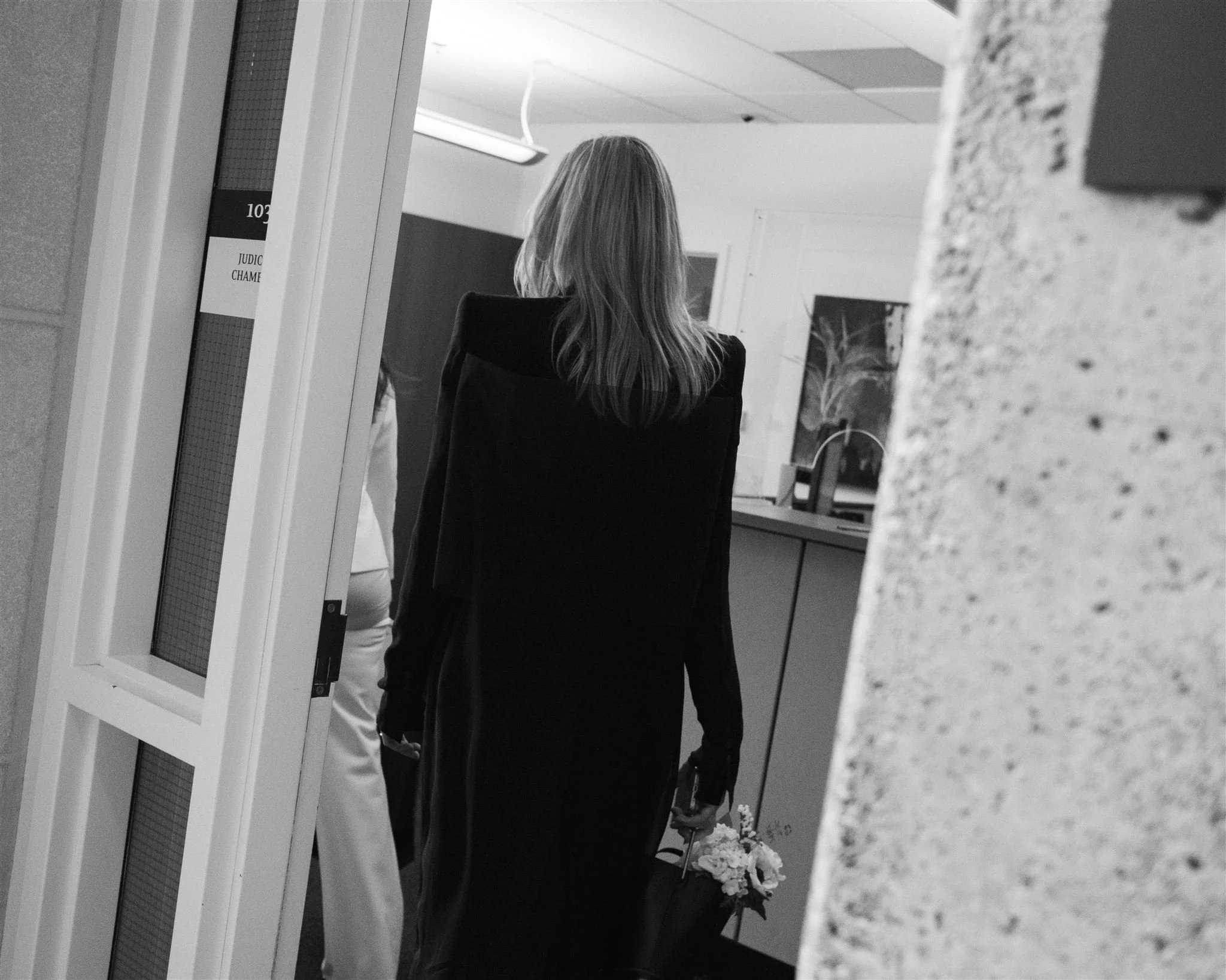 Guest walking into a courtroom at the Seattle Municipal Courthouse holding flowers, photographed in black and white during an intimate wedding ceremony.