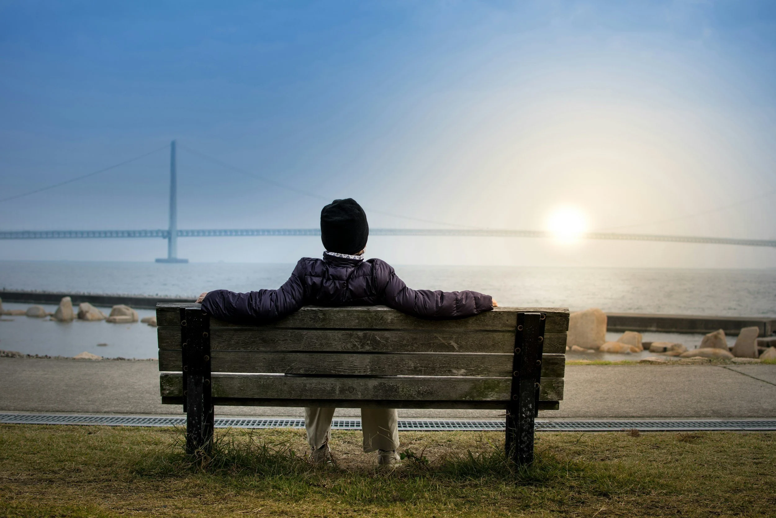 Person sitting on a bench facing the sun and a bridge contemplating first responder therapy