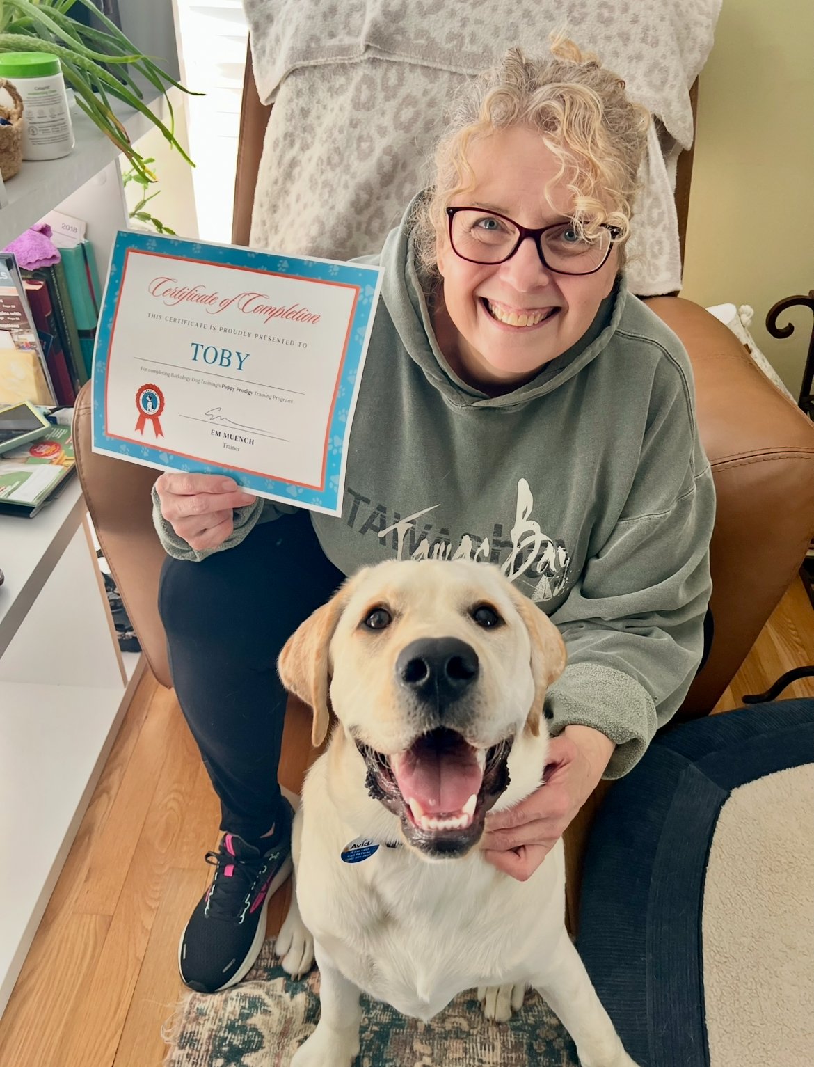 a woman poses with her dog and their dog training certificate of completion