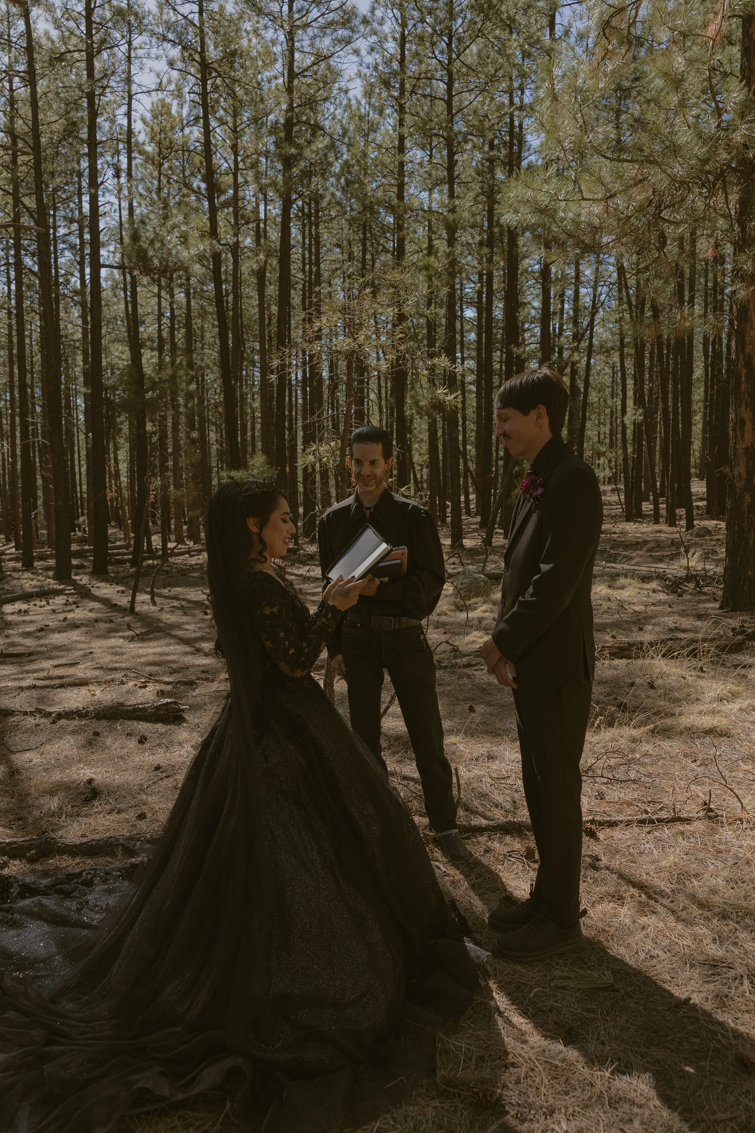 A couple getting married outdoors in a forest, with an officiant reading from a book.