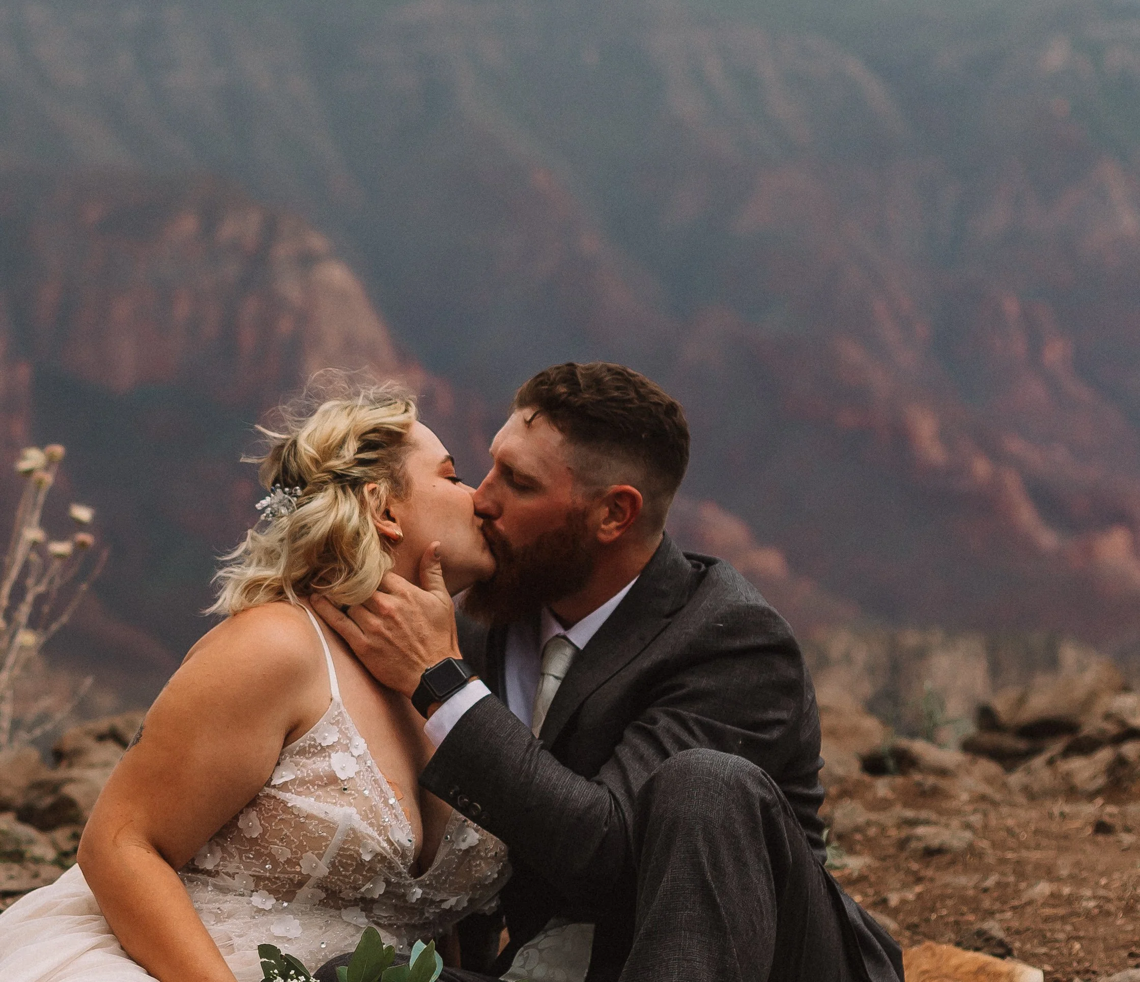 A couple in wedding attire kissing, with a mountainous landscape in the background.