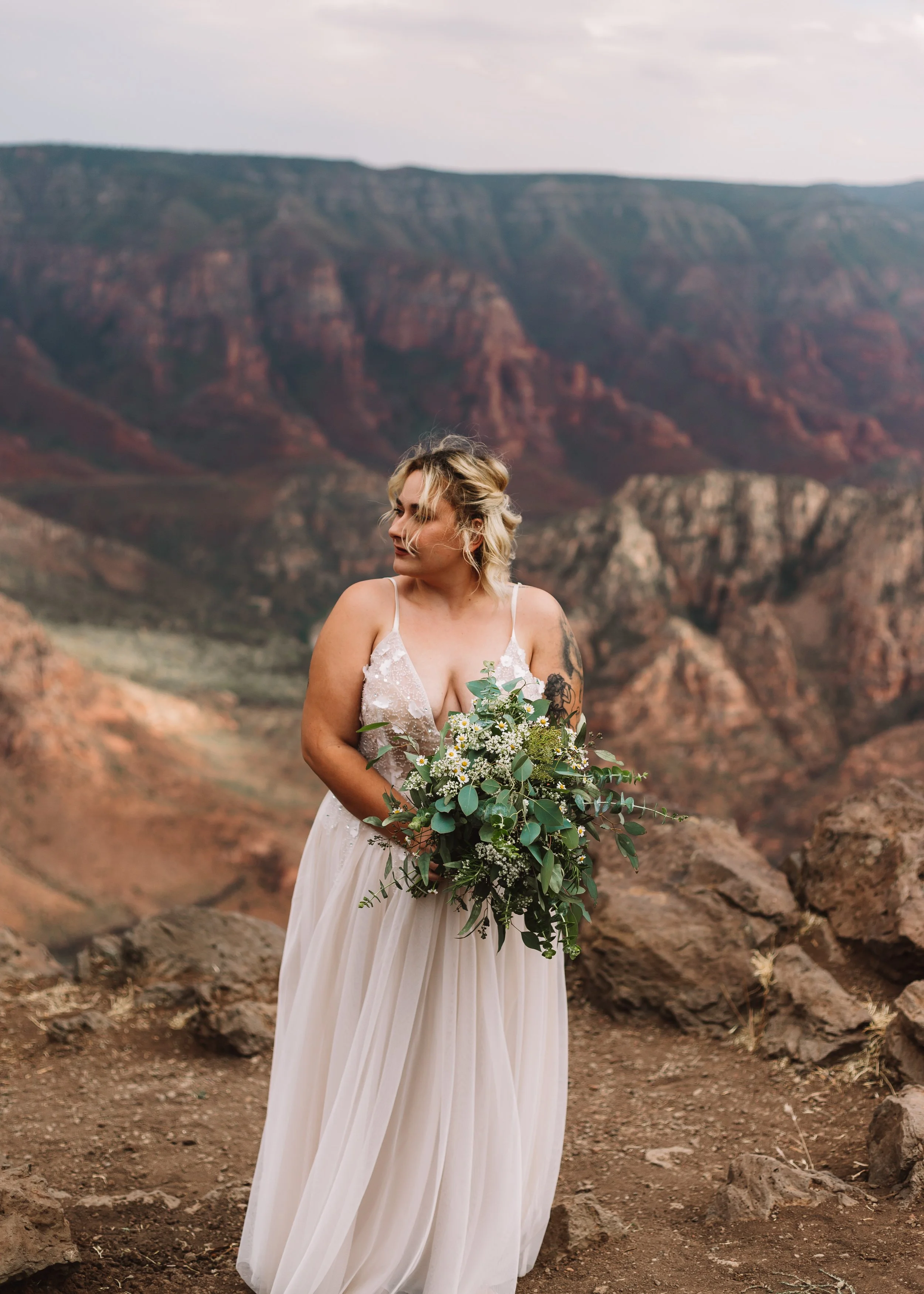 Bride in a white gown holding a bouquet in a mountainous landscape.