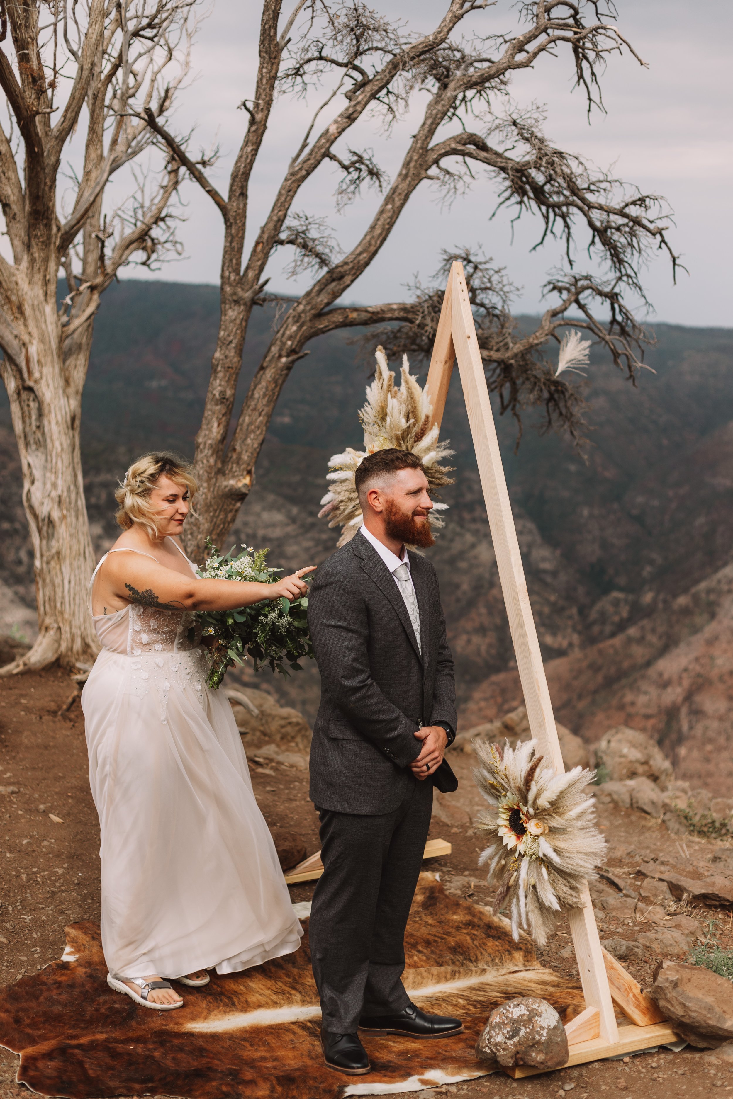 Bride sneaking up on groom for a first look during an outdoor wedding ceremony with rustic decorations.