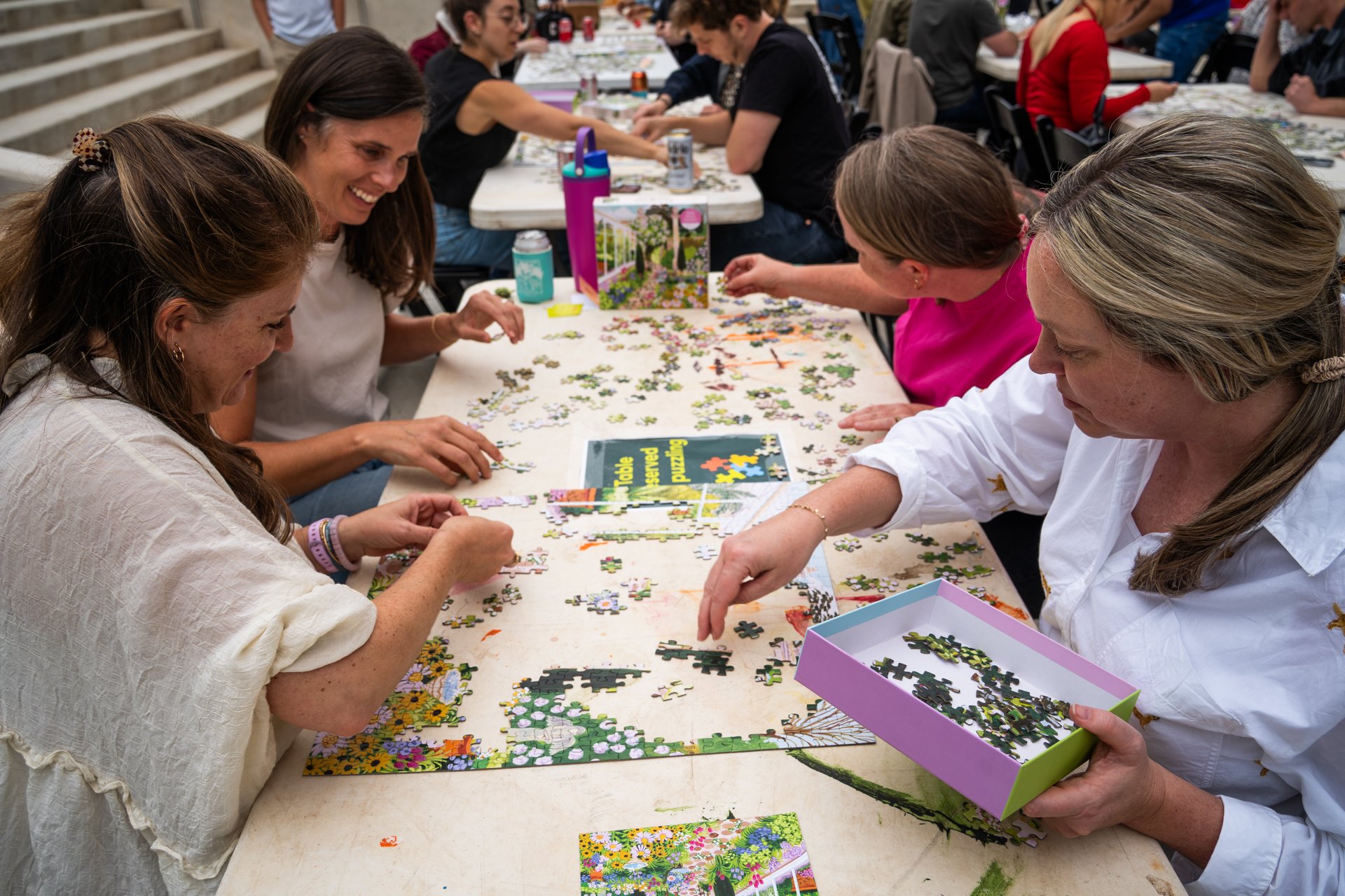 People working together on a large jigsaw puzzle at a table in an indoor setting.