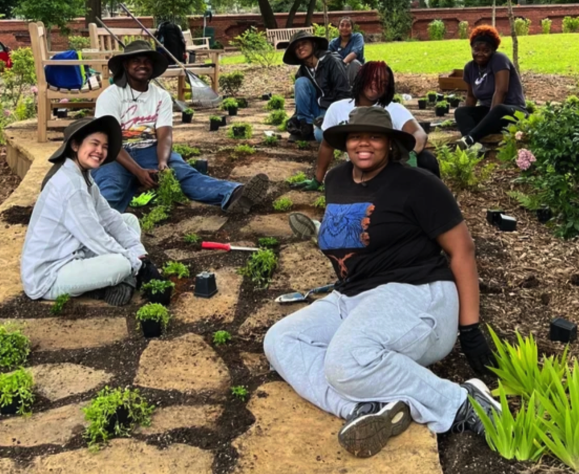 Group of women and girls gardening outdoors, planting and caring for plants in a community garden.