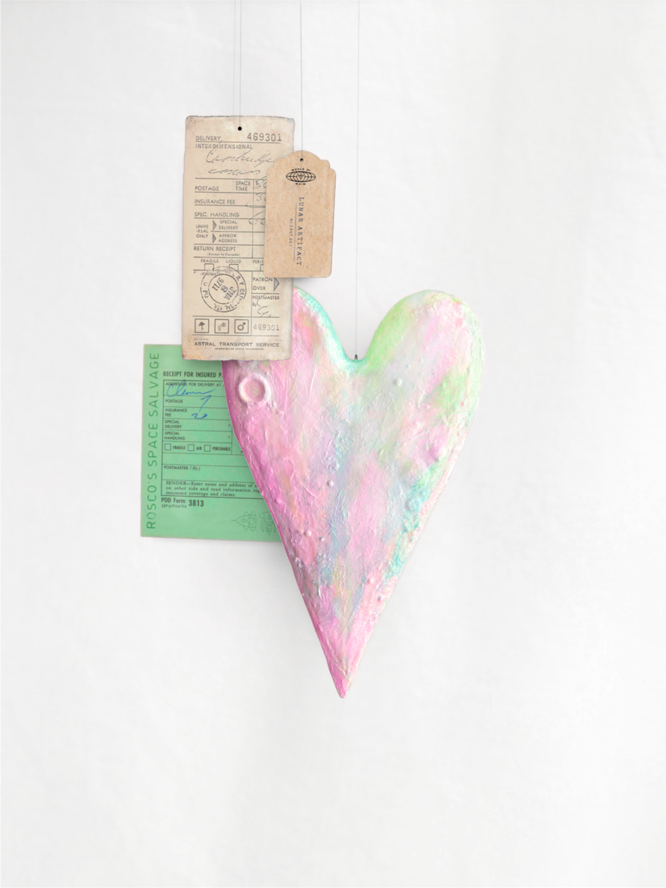 Pink and pastel-colored heart-shaped object with a green space salvage receipt and vintage tags attached, on a plain white background.