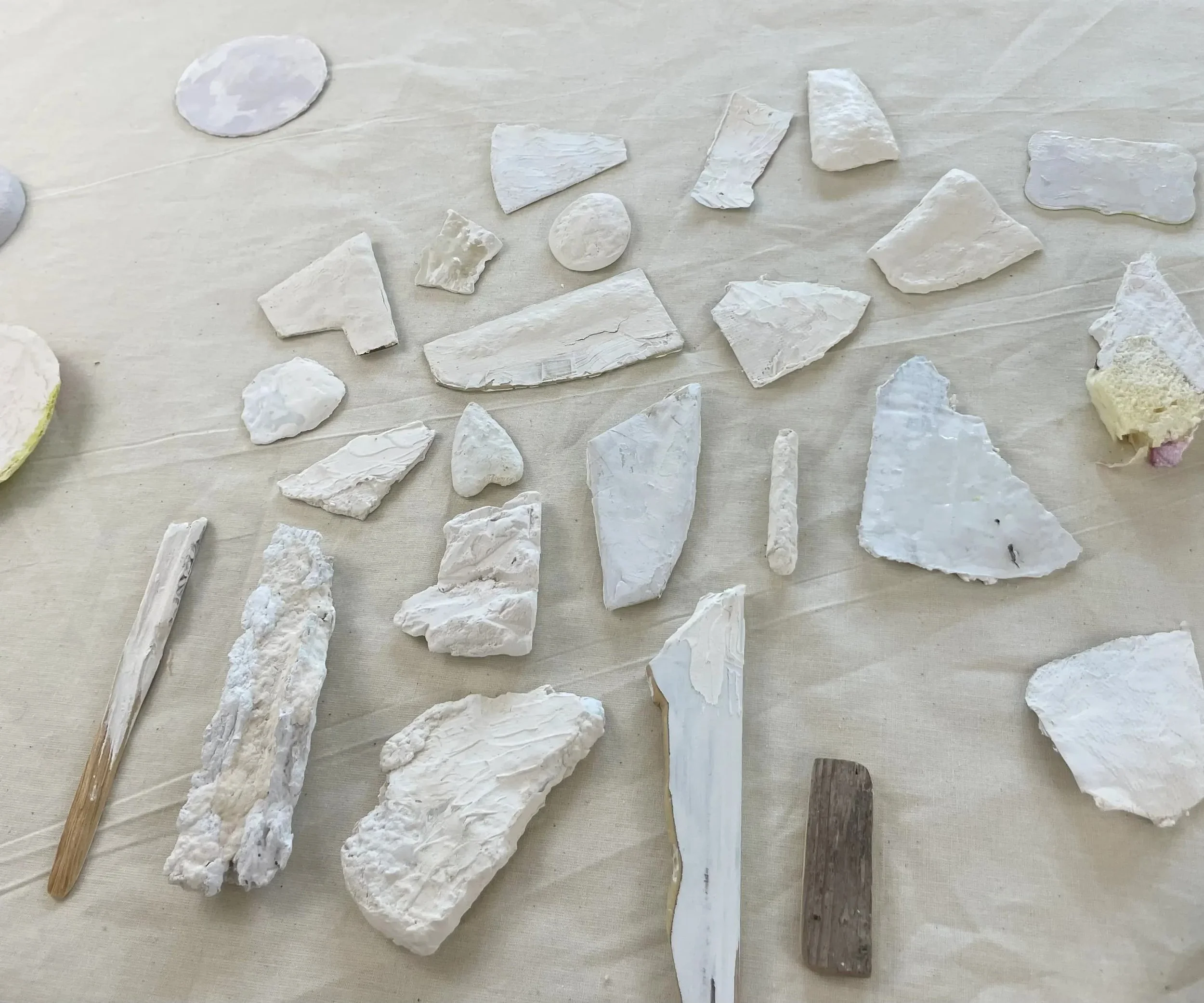 Collection of ghostly white stones and rocks, some with a chalky appearance, laid out on a flat, light-colored surface, with two wooden sticks among them.