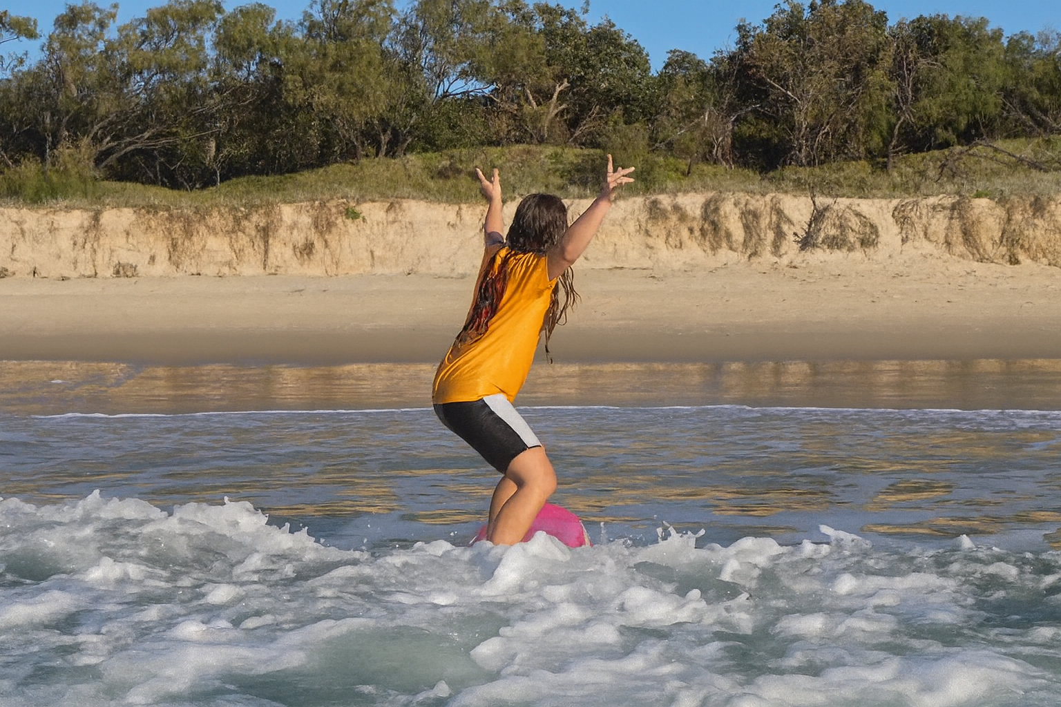"Beginner surf student performing a 'claim' after catching a wave during a Send It Surf Academy kids lesson at Peregian Beach, Sunshine Coast."