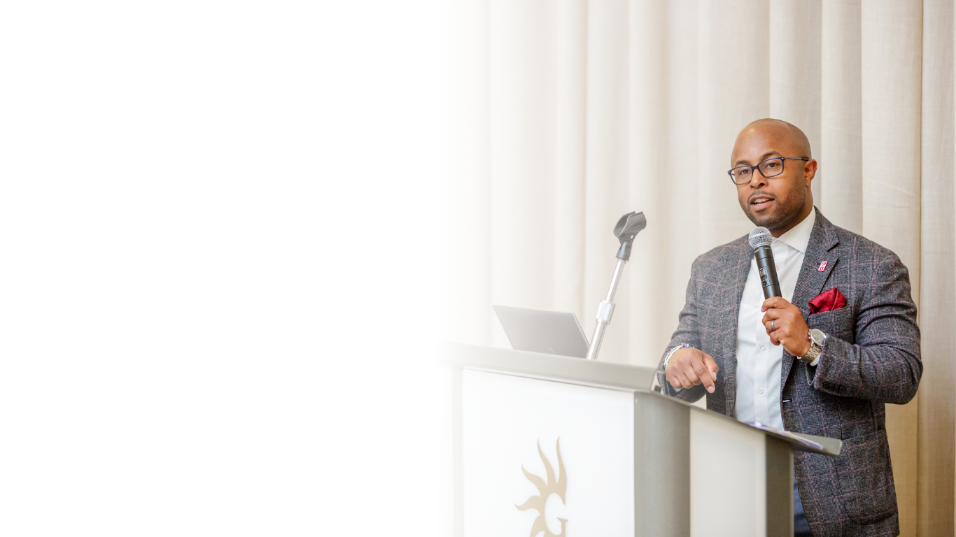 This is Dr. Dexter Shorter in a gray suit and glasses giving a speech at a podium with a microphone.