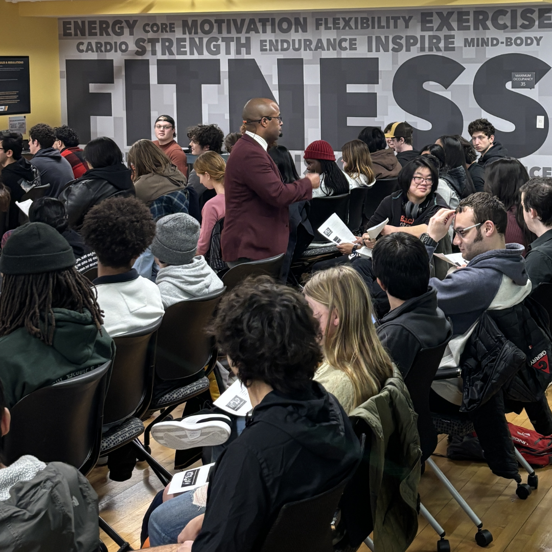 This is Dr. Dexter Shorter speaking to a group of UMBC students. The wall behind features large words related to fitness and motivation, with a bright yellow wall on the side.