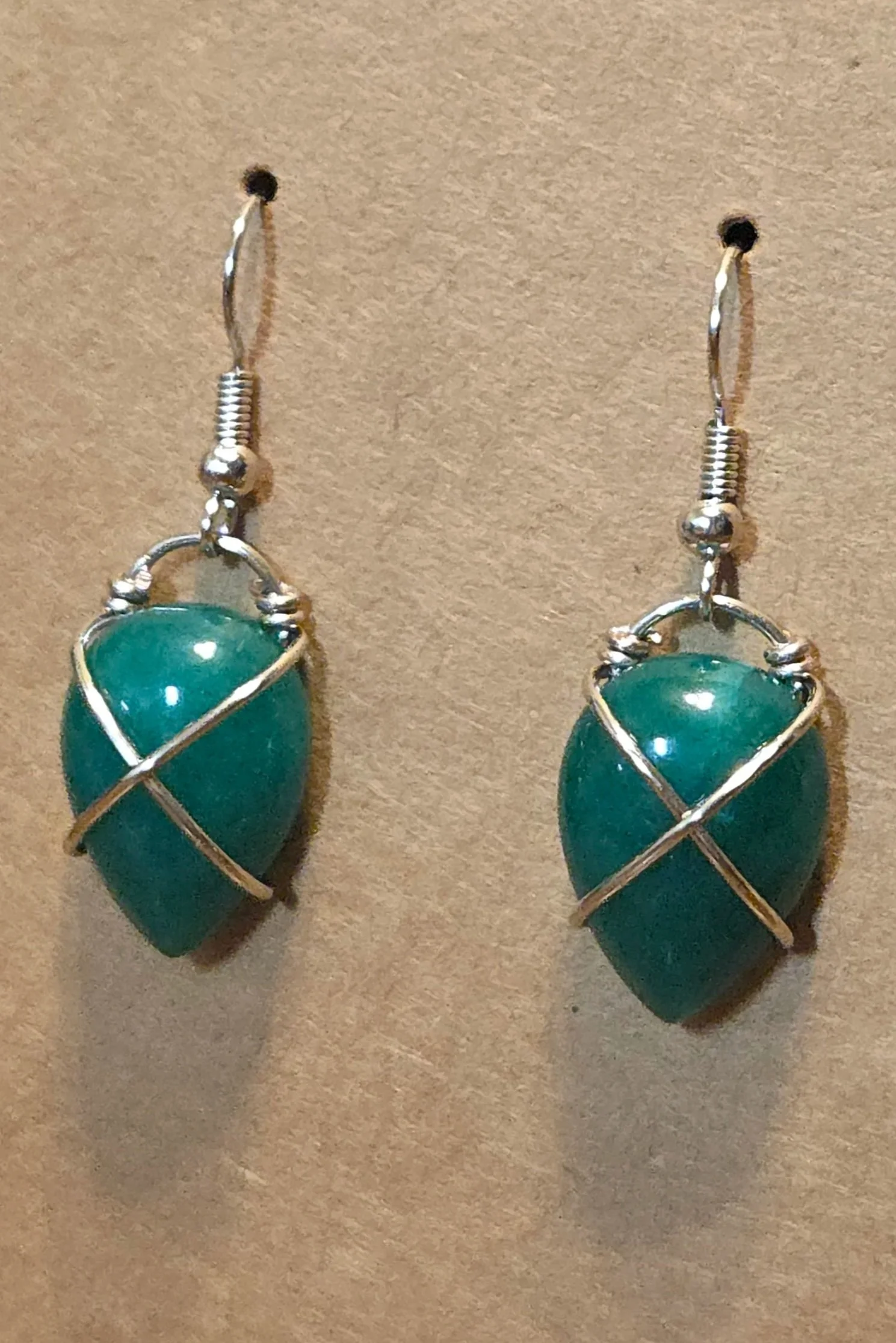 Silver earrings with green, oval-shaped stones wrapped in silver wire.