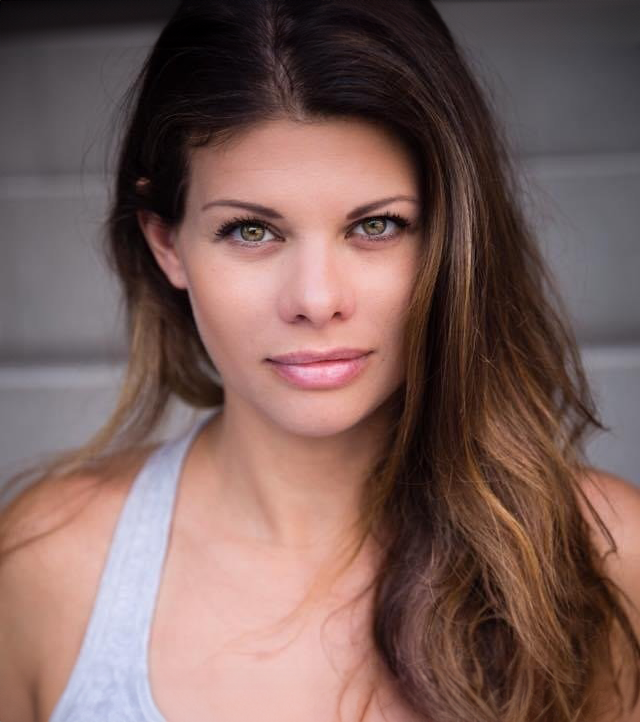 Young woman with long brown hair and a gray tank top, looking at camera.