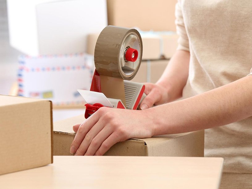 A person carefully sealing a cardboard package with tape.