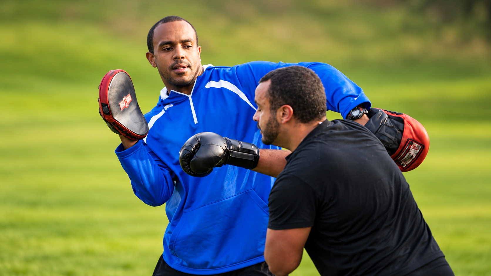Boxing coach working focus mitts with an athlete during an outdoor training session.
