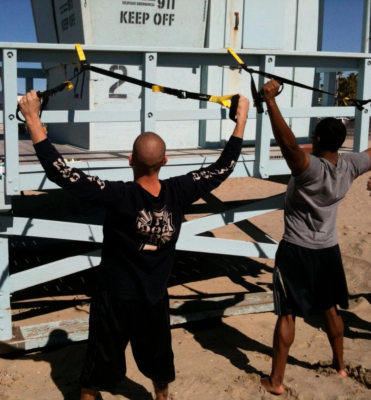 Two athletes performing TRX suspension training exercises during an outdoor strength and conditioning workout.