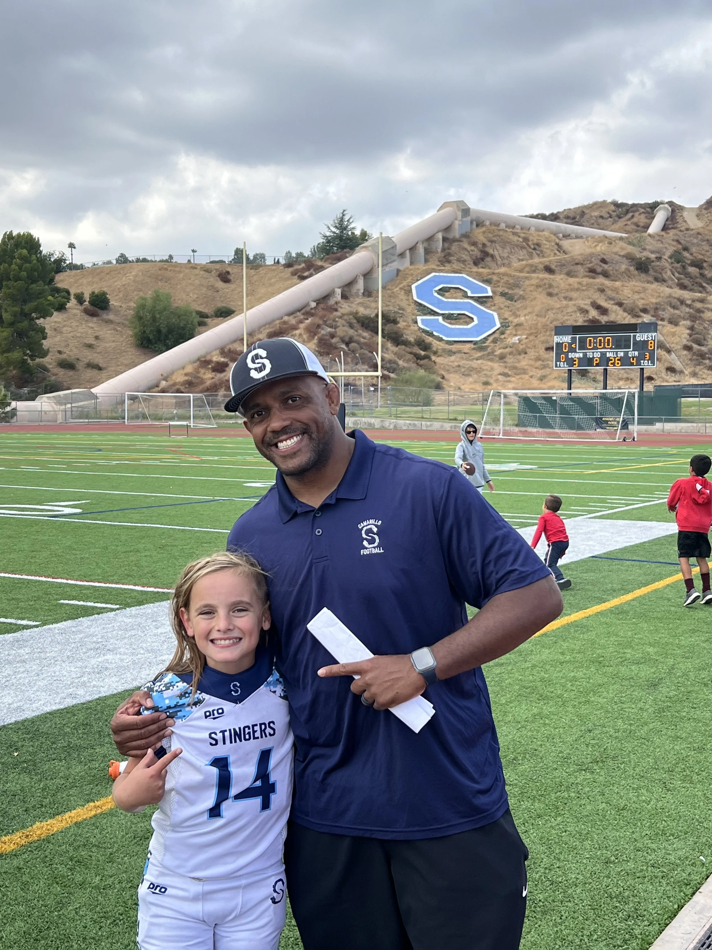 Football coach mentoring a young athlete during a training session on a football field.
