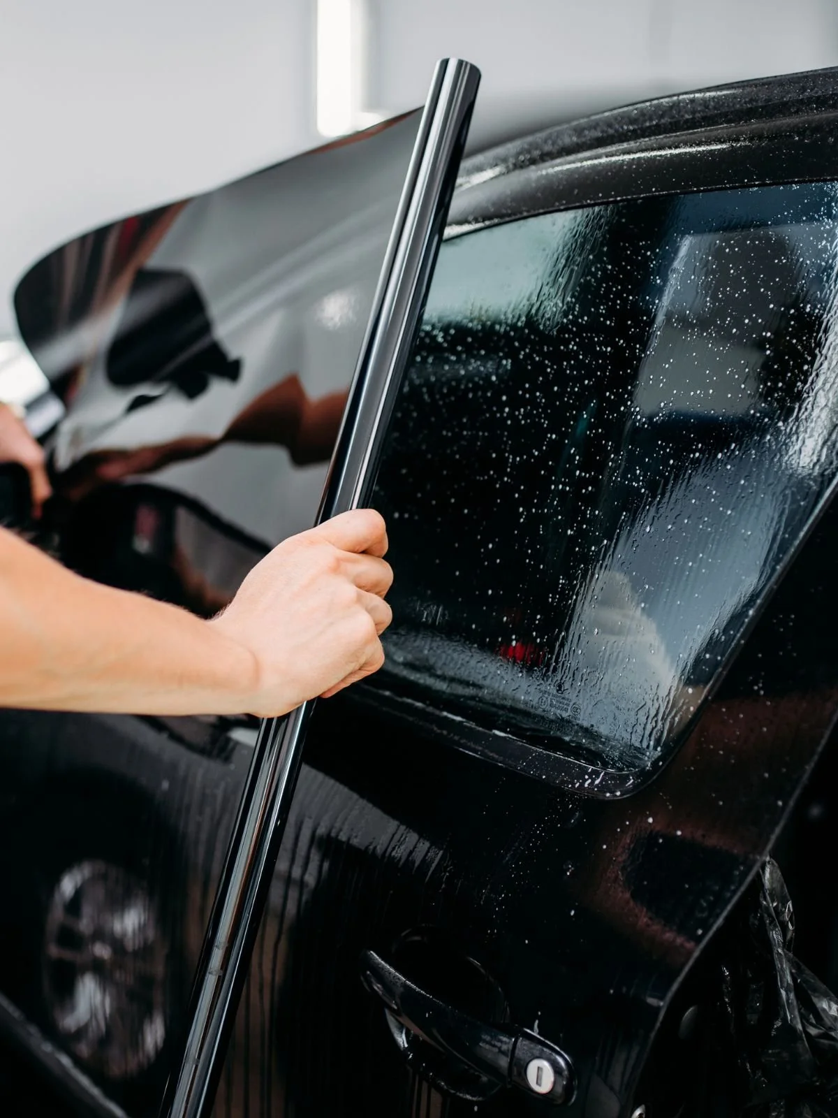 Person cleaning or applying a streak-free coating to a car's side window with a squeegee.