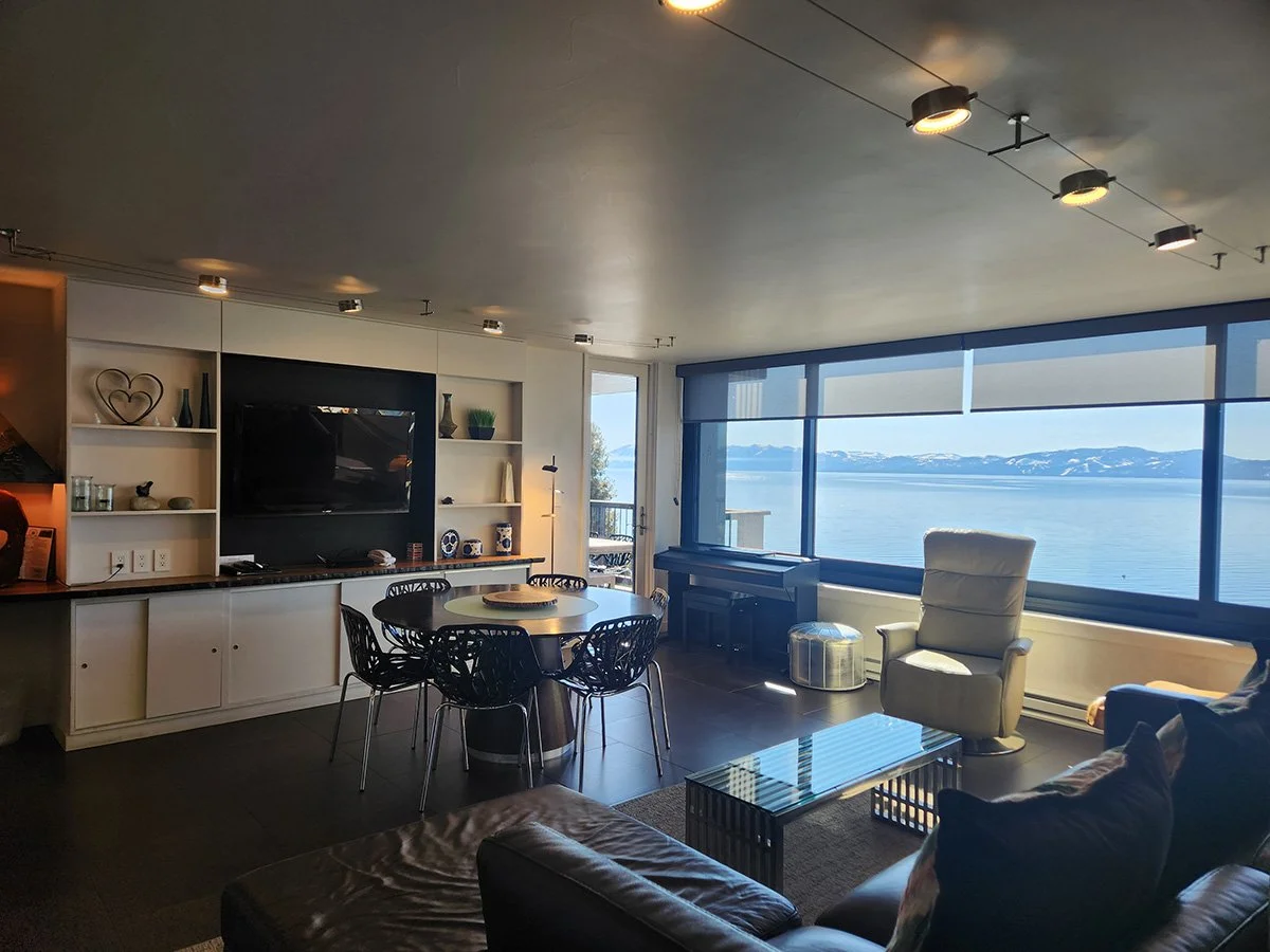 living room with view of lake through large windows, round dining table, dark leather sofa, cabinet with tv