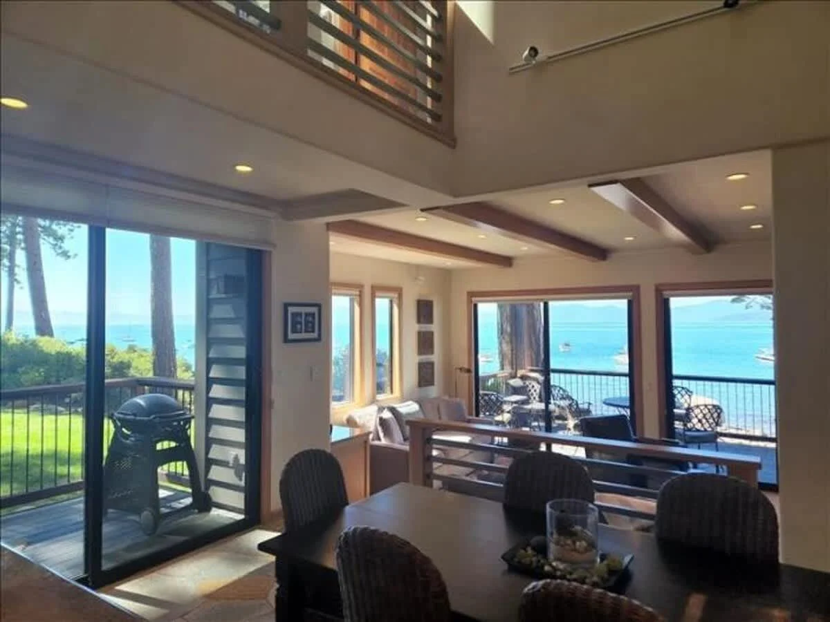 dining area off deck with dark wood table and 6 cane chairs, shows view of lake through living room doors