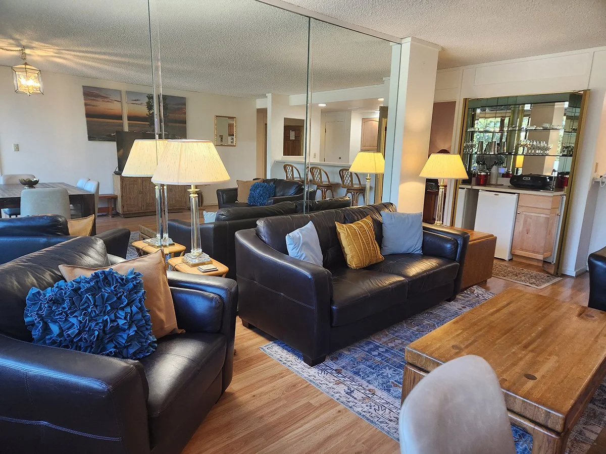 living room showing wood floor, leather couches, dining table, oriental-style area rug, mirrored wall behind couch